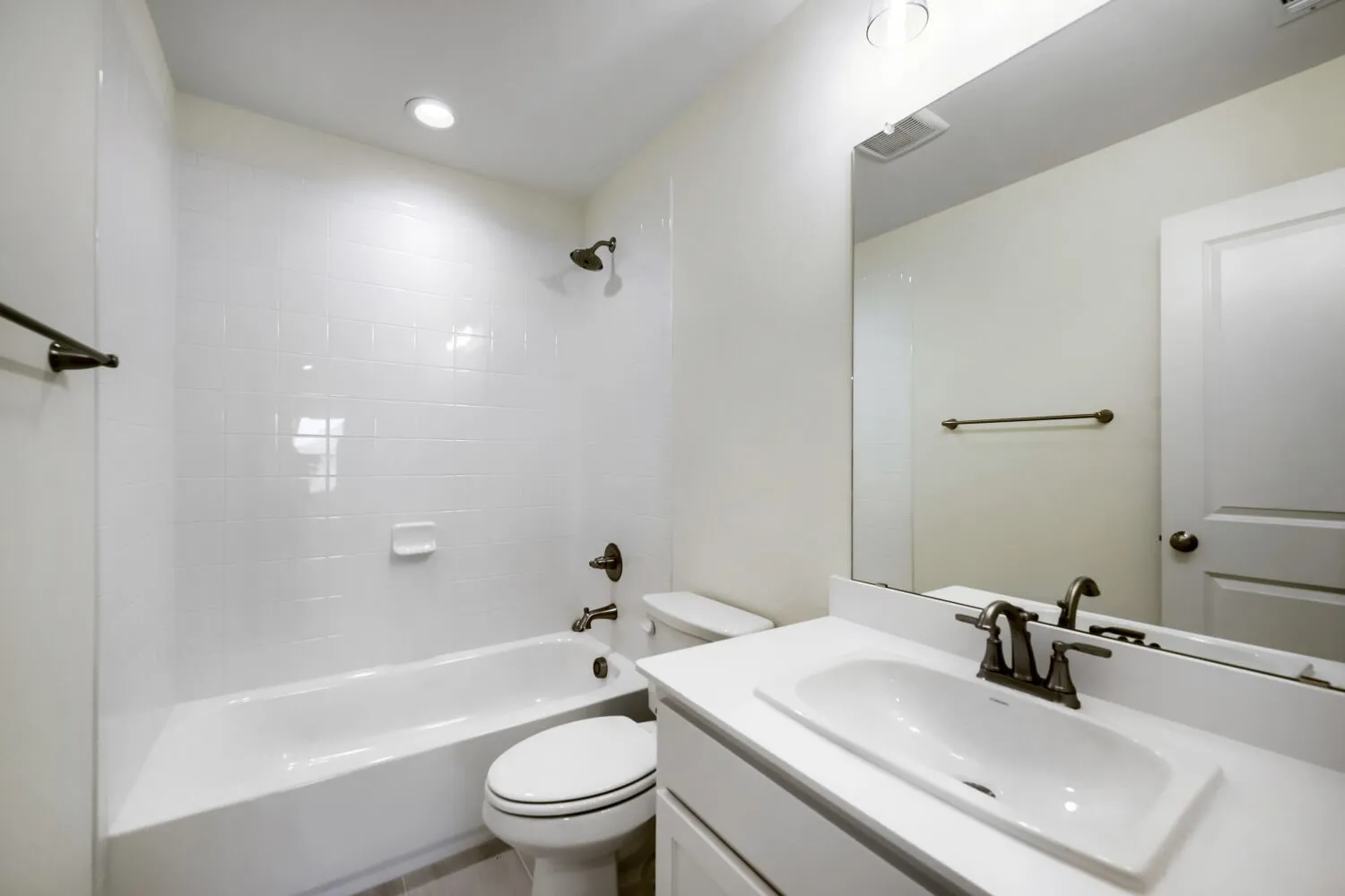 Bright bathroom featuring a white tub and shower combination with subway tile surround, single vanity with integrated sink, and bronze fixtures