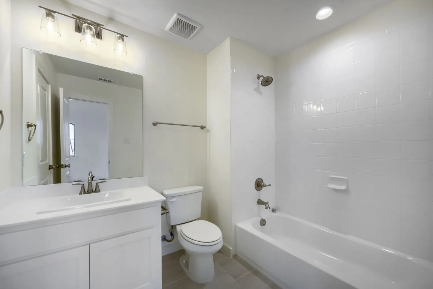 Bathroom featuring a white vanity with integrated sink, brushed nickel fixtures, a rectangular mirror, a toilet, and a bathtub with white subway tile surround