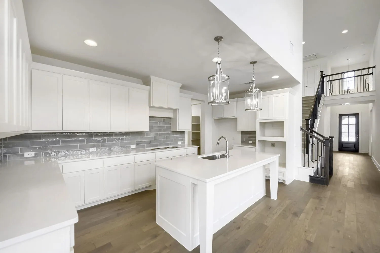 Contemporary kitchen featuring white cabinetry, light-toned countertops, a full-height gray tile backsplash, and wood-finish flooring