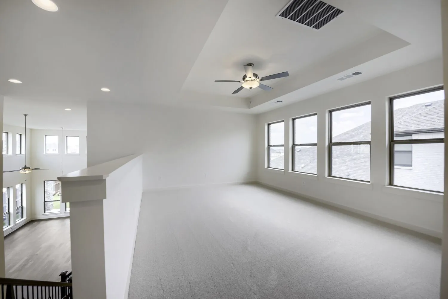 Spacious upper-level area featuring a tray ceiling with a ceiling fan and recessed lighting, multiple windows, and light-toned carpeting