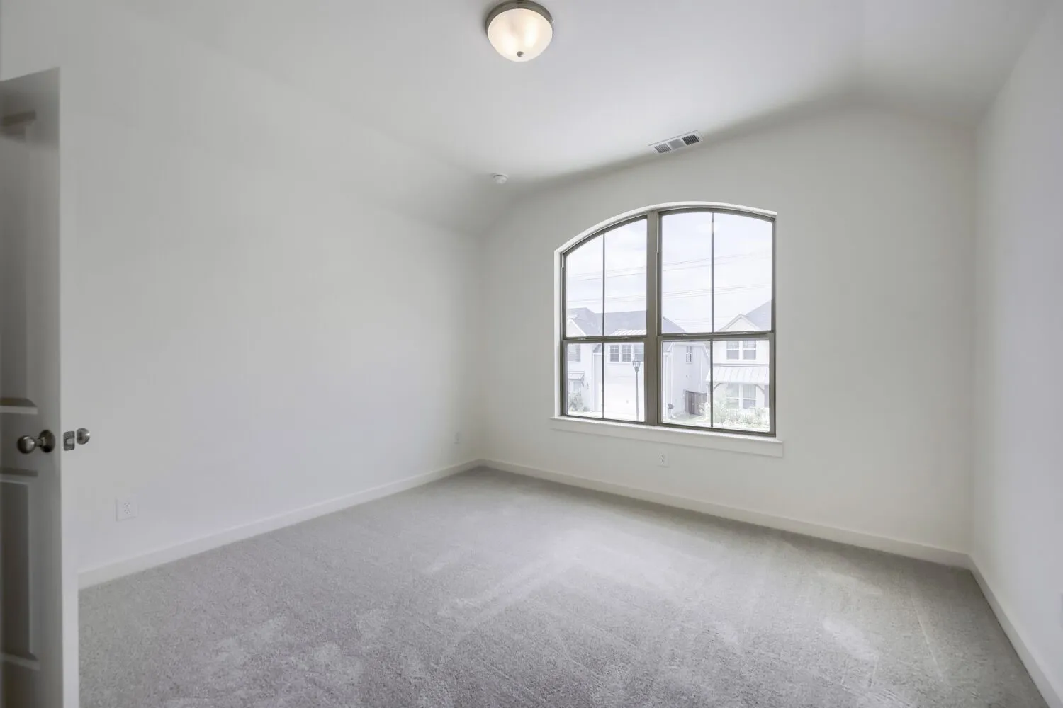 Room featuring an arched window, vaulted ceiling, neutral wall paint, and gray carpeting