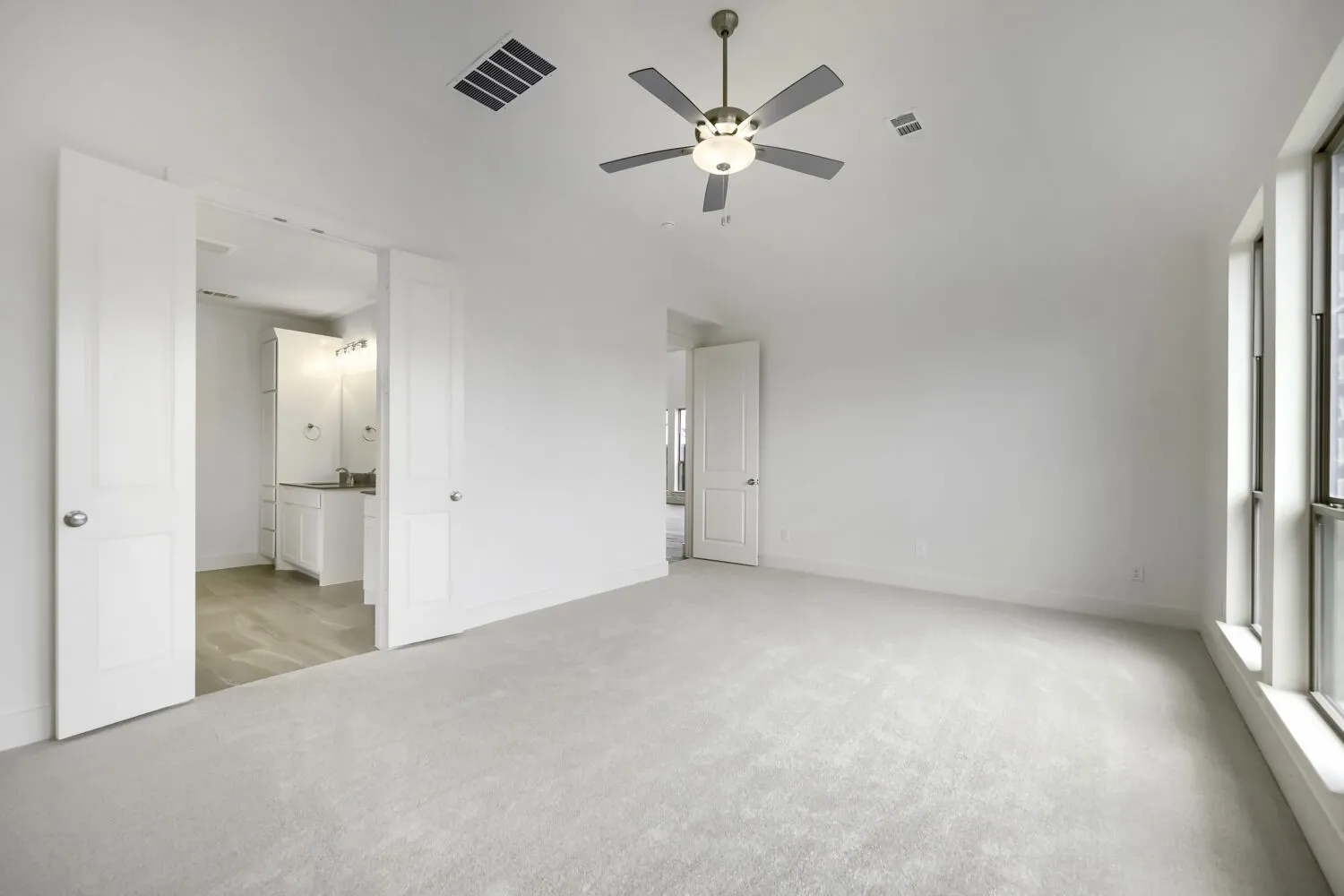 Spacious room featuring light-colored carpeting, multiple large windows, and a ceiling fan with integrated lighting