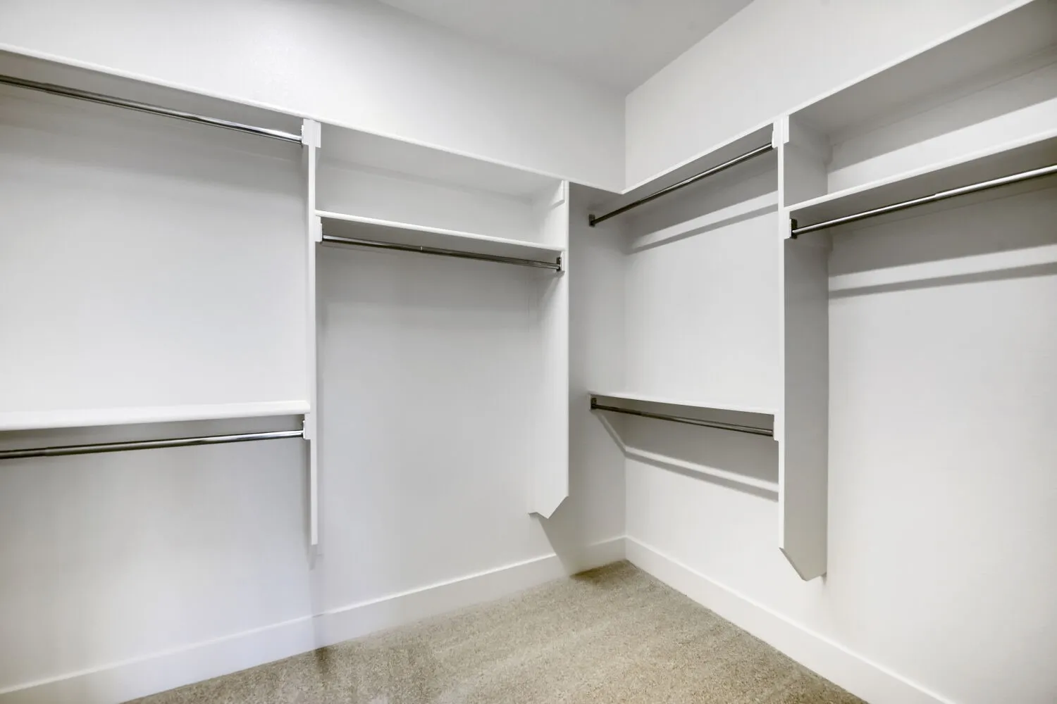 Walk-in closet featuring white built-in shelving, multiple hanging rods, and light-toned carpet flooring