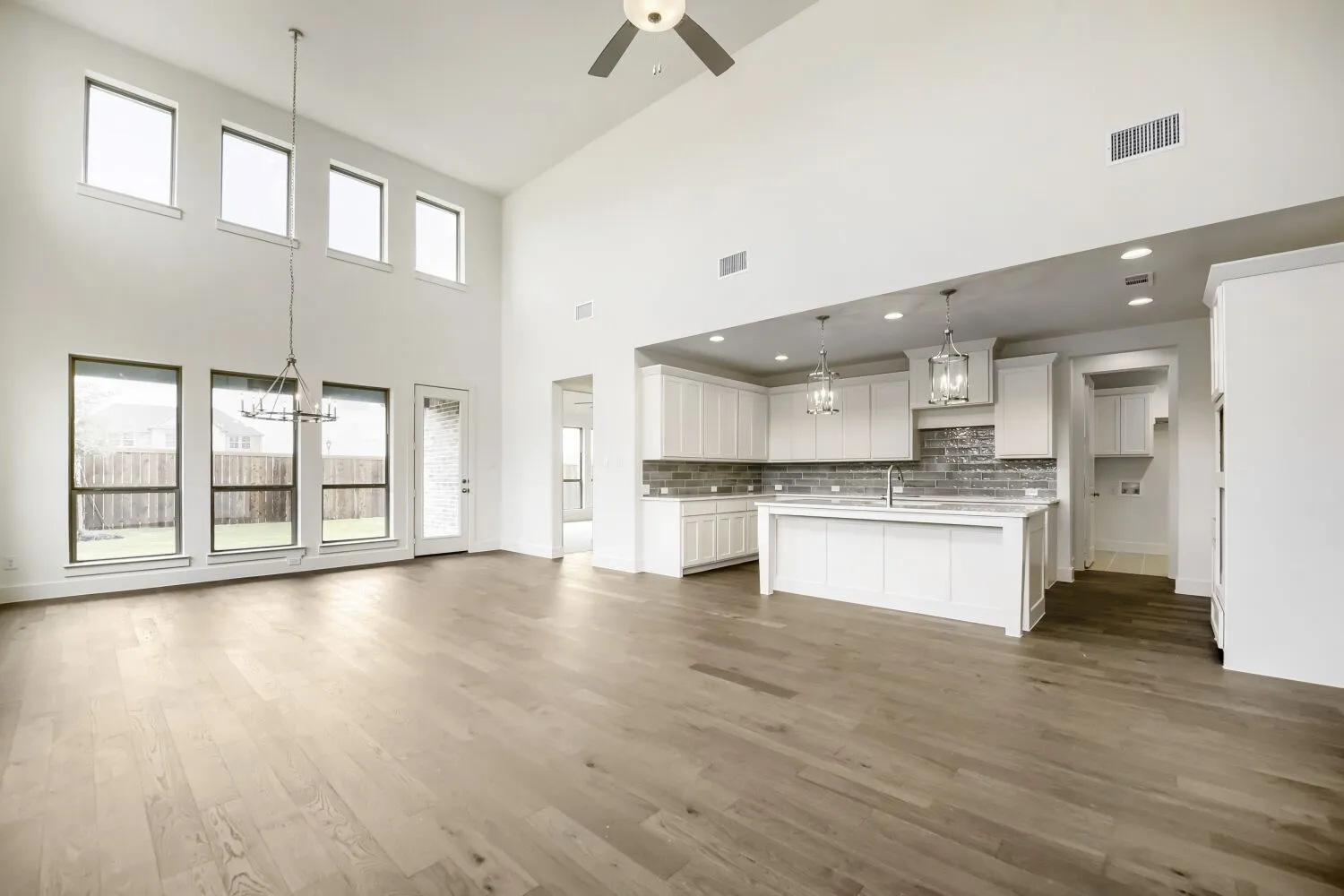 Spacious room featuring soaring ceilings, wood-finish flooring, and a kitchen with white cabinetry, a large island, and subway tile backsplash
