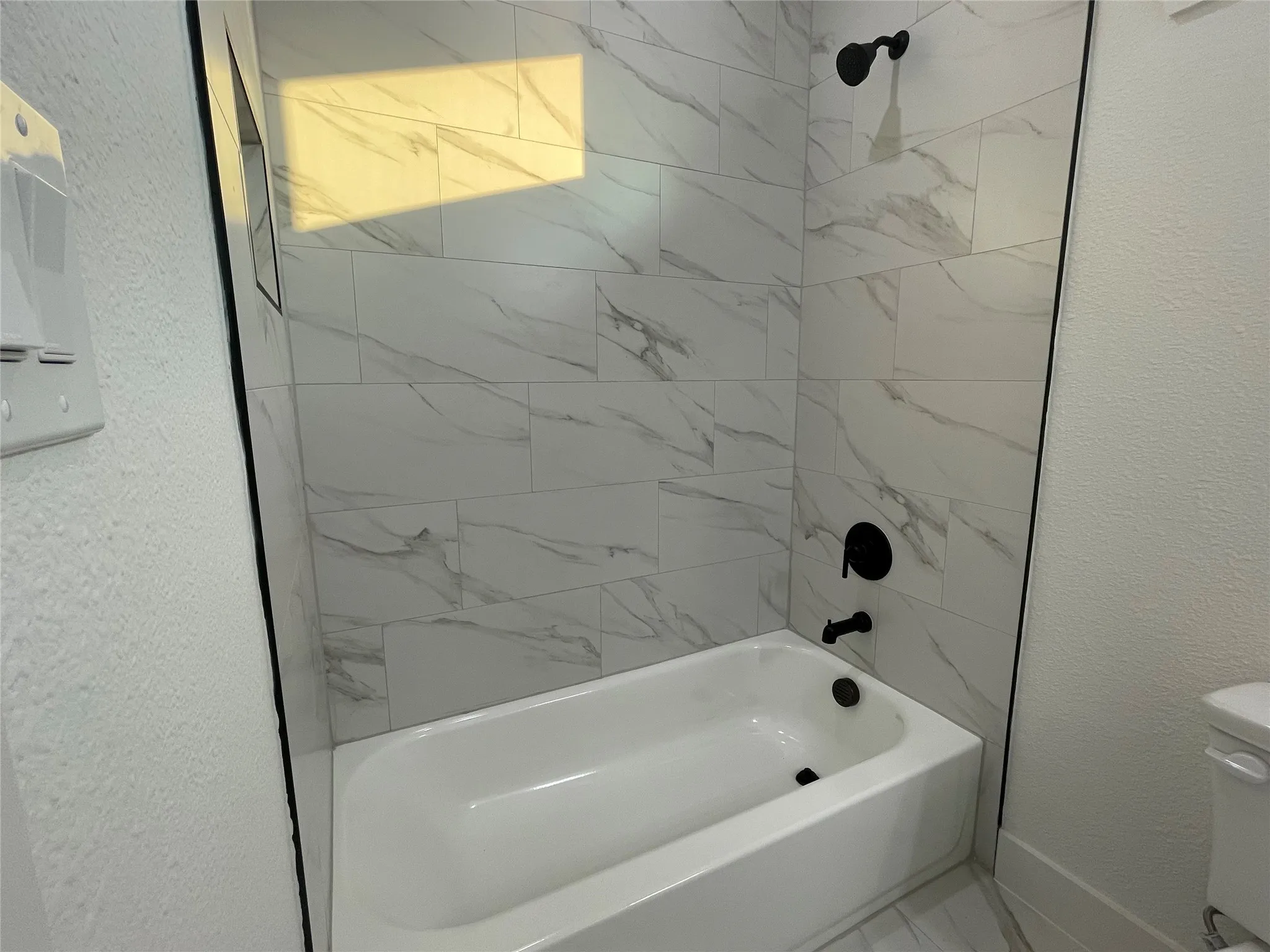 Full bathroom featuring a textured wall and shower / tub combination