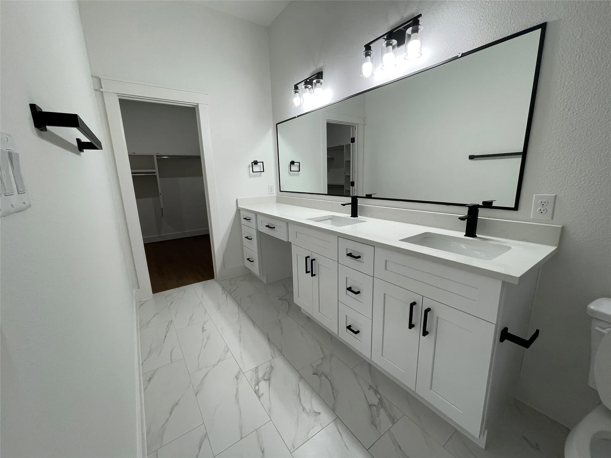 Bathroom with a walk in closet, double vanity, and light marble finish floors