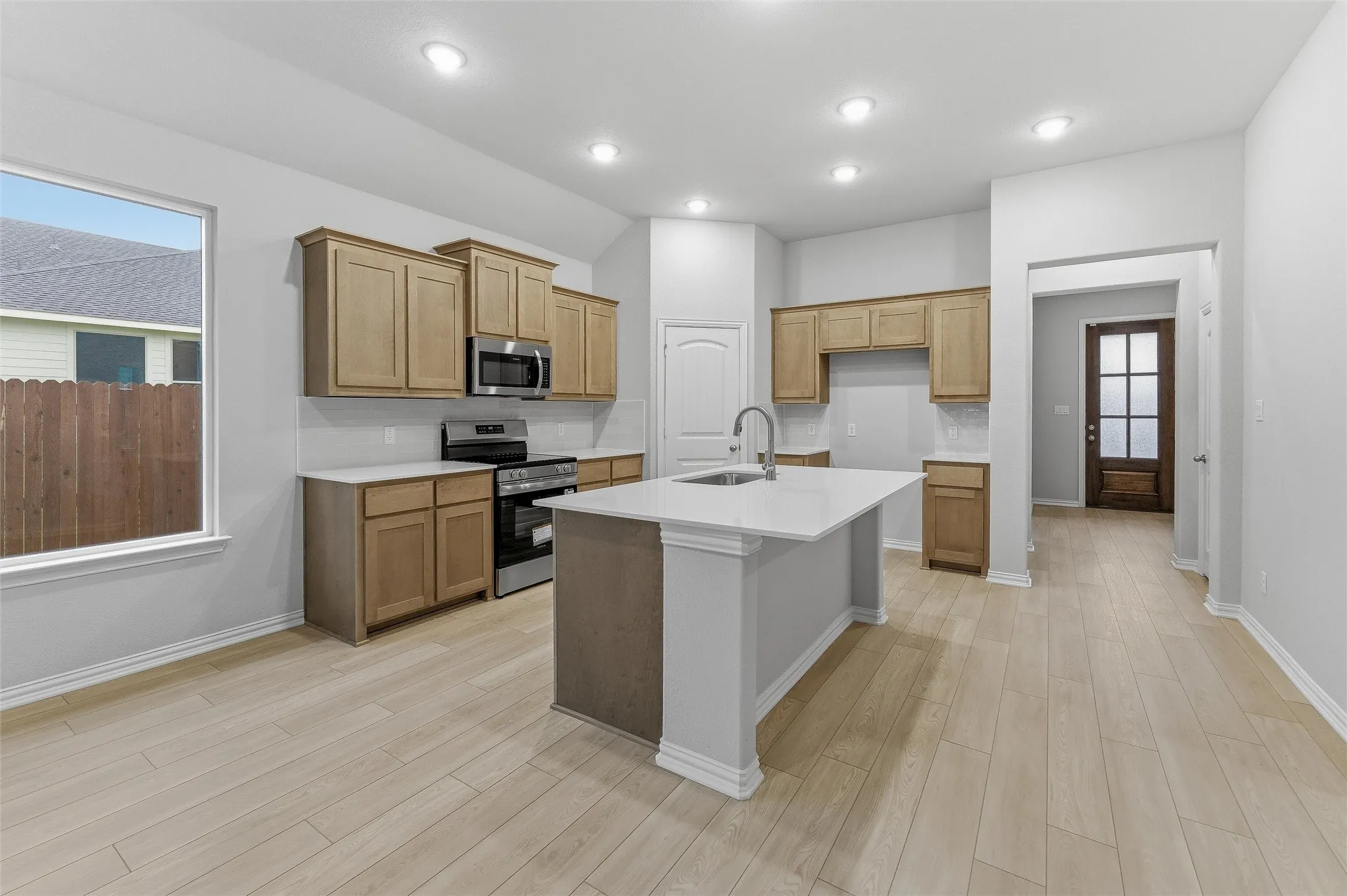 Kitchen featuring a central island with an undermount sink, light wood-finish cabinetry, stainless steel appliances, and wood-finish flooring