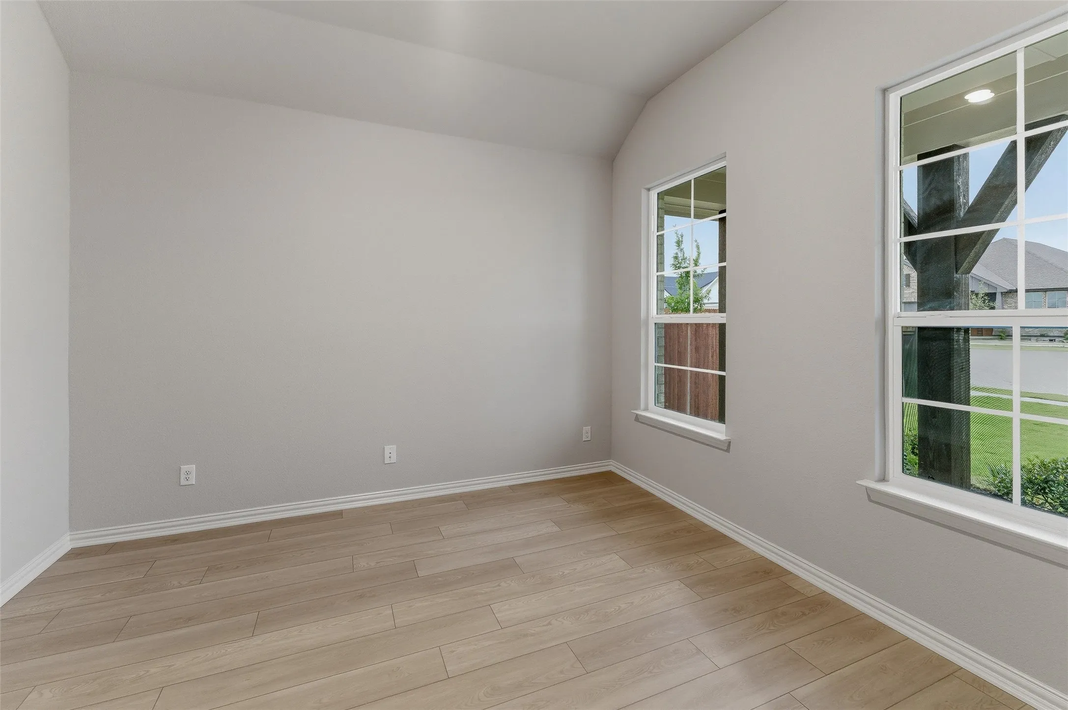 Room featuring light gray walls, wood-finish flooring, white baseboards, and two windows with white grilles