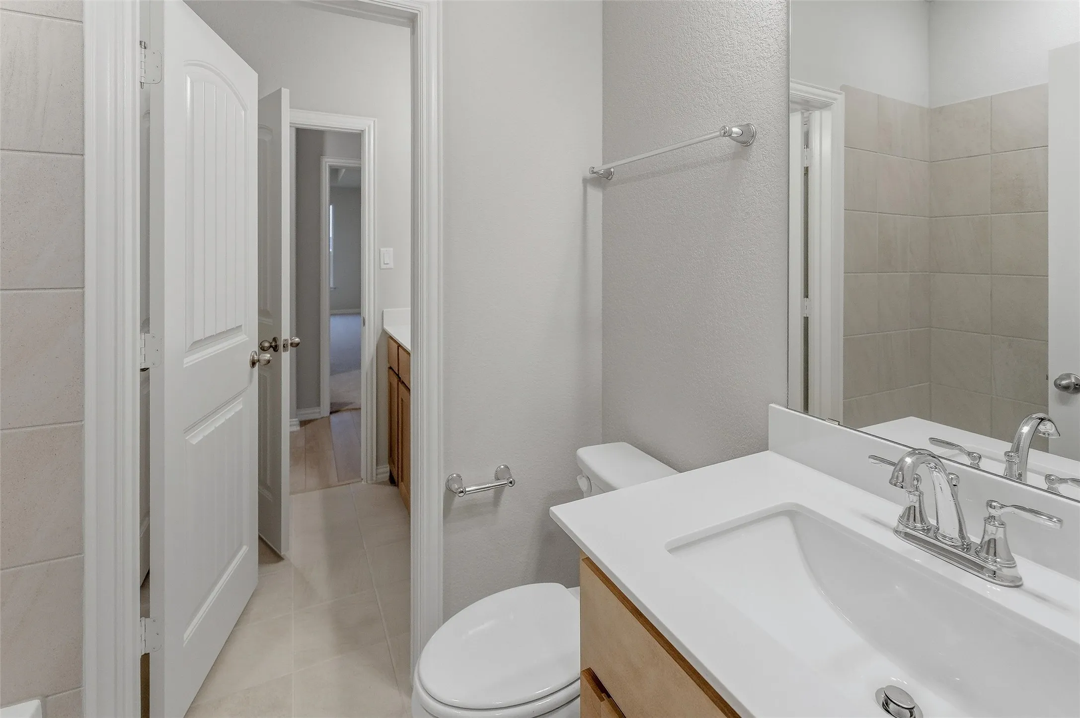 Bathroom featuring a light wood-finish vanity with a white countertop and integrated sink, chrome faucet, and expansive wall mirror