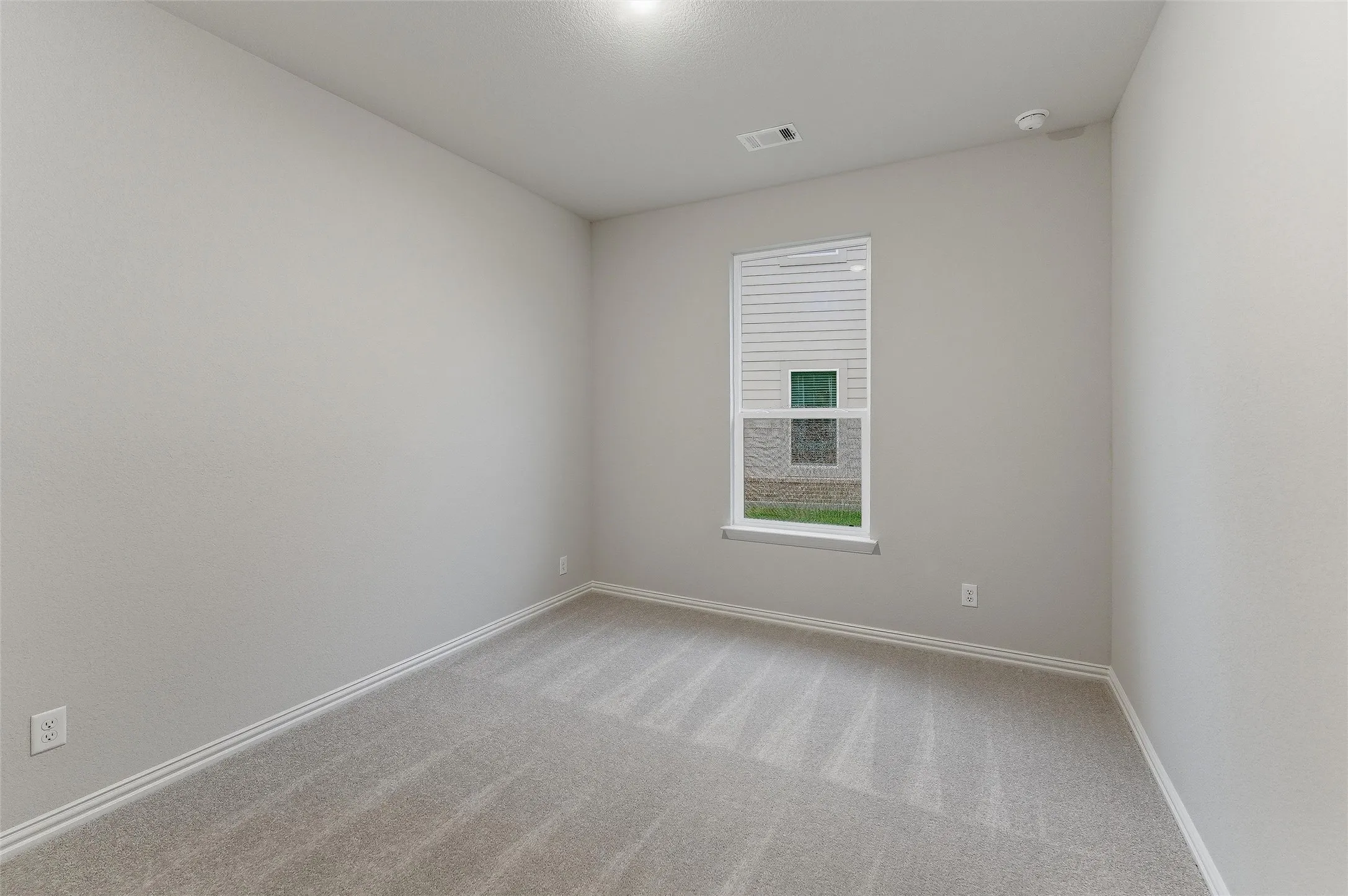 Neutral tone walls and carpeting throughout a room featuring a single window with blinds, baseboard trim, and a ceiling-mounted light fixture