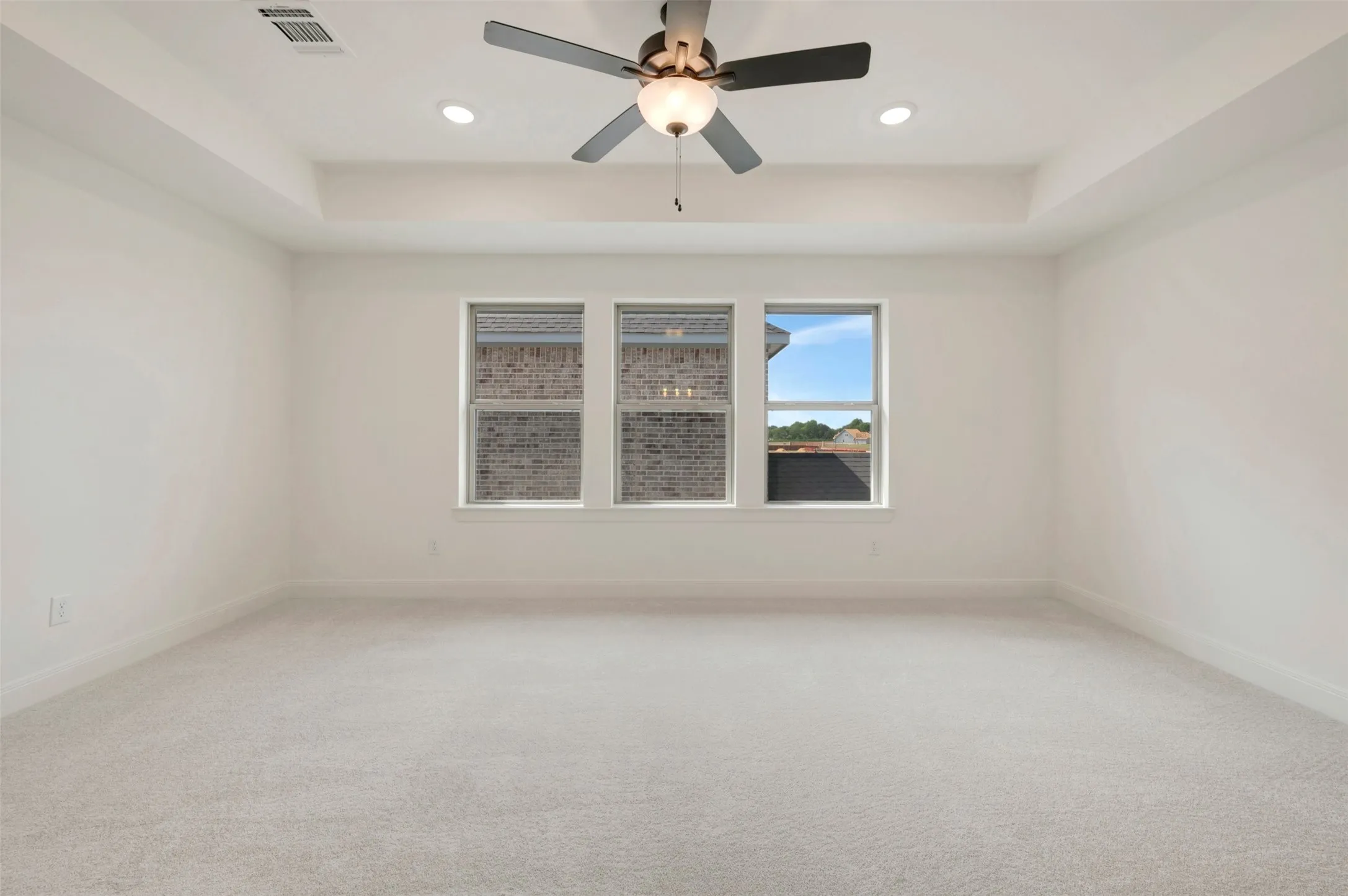 Spacious interior featuring light-toned carpeting, white walls, a tray ceiling, and a ceiling fan with integrated lighting