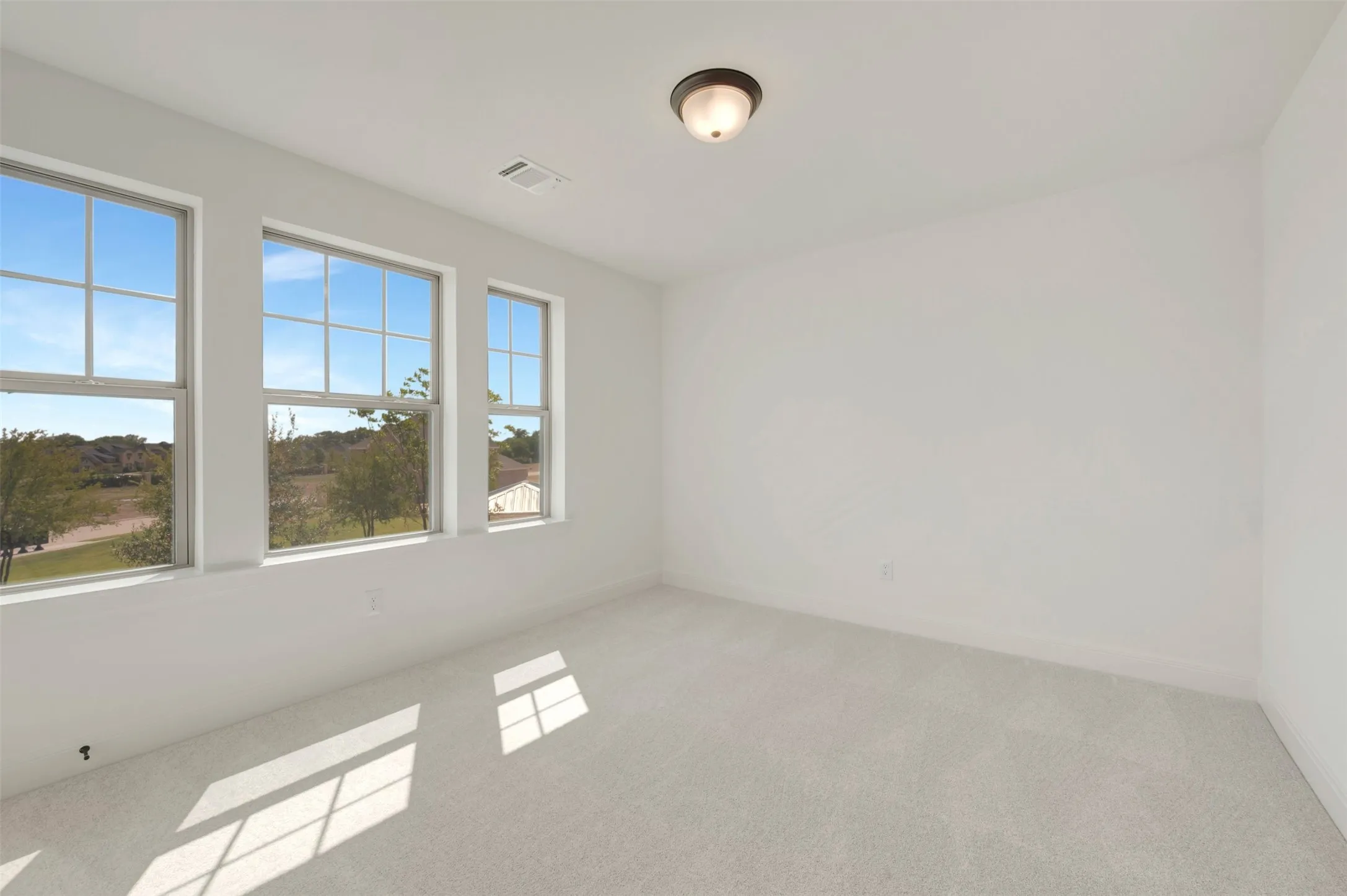 Room featuring three large vertical windows, light gray carpeting, neutral wall color, and a ceiling-mounted light fixture