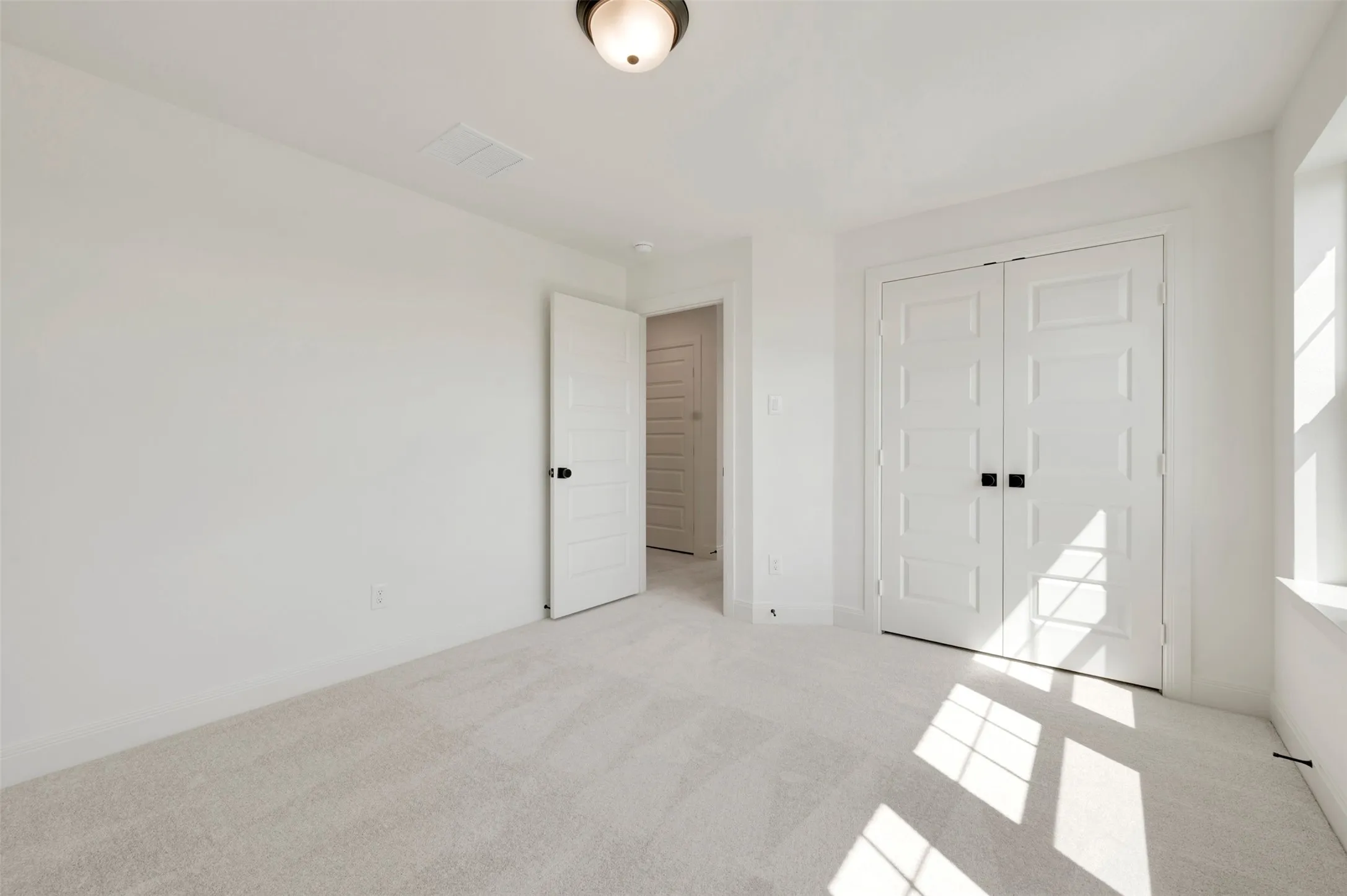Neutral-toned carpeting and light walls define this space, featuring a double-door closet with dark hardware