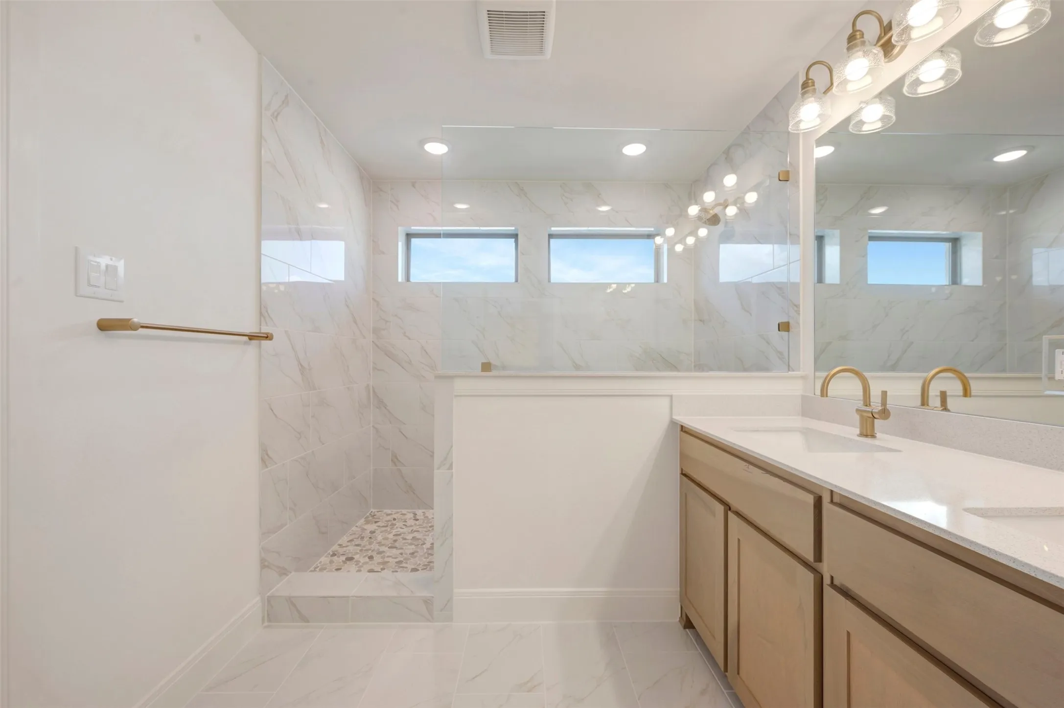 Contemporary bathroom featuring a large walk-in shower with a glass enclosure, white marble-style tile, and a pebble-stone shower floor