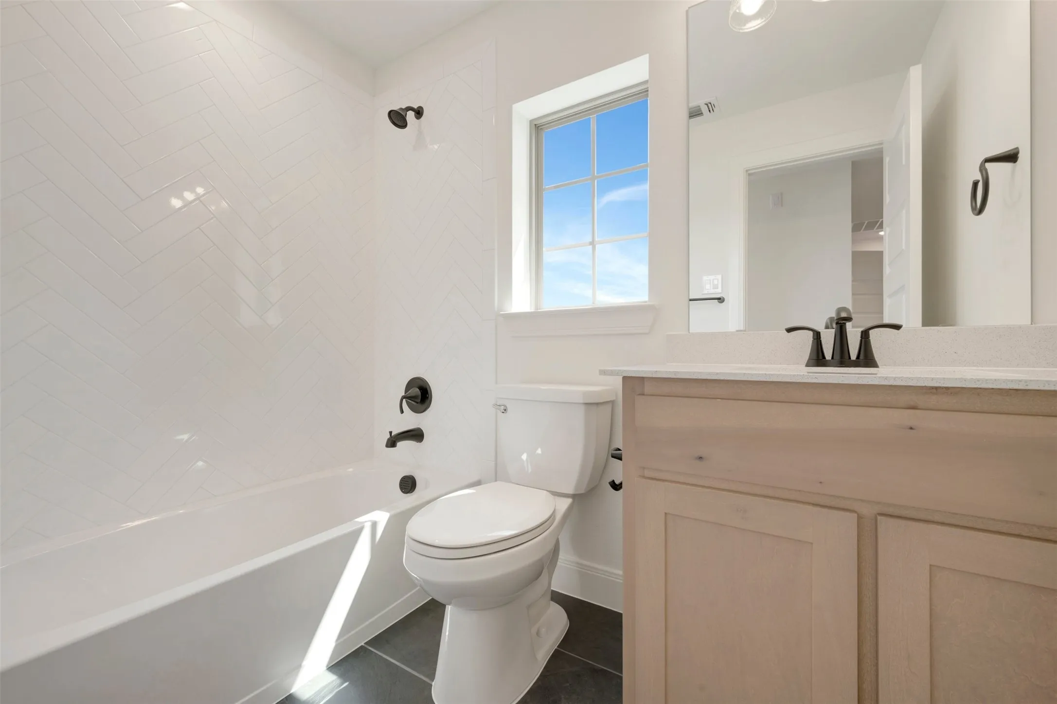 Bathroom featuring a built-in tub with white subway tile surround in a herringbone pattern, a vanity with a light-toned cabinet and light-colored countertop, and dark-finish fixtures