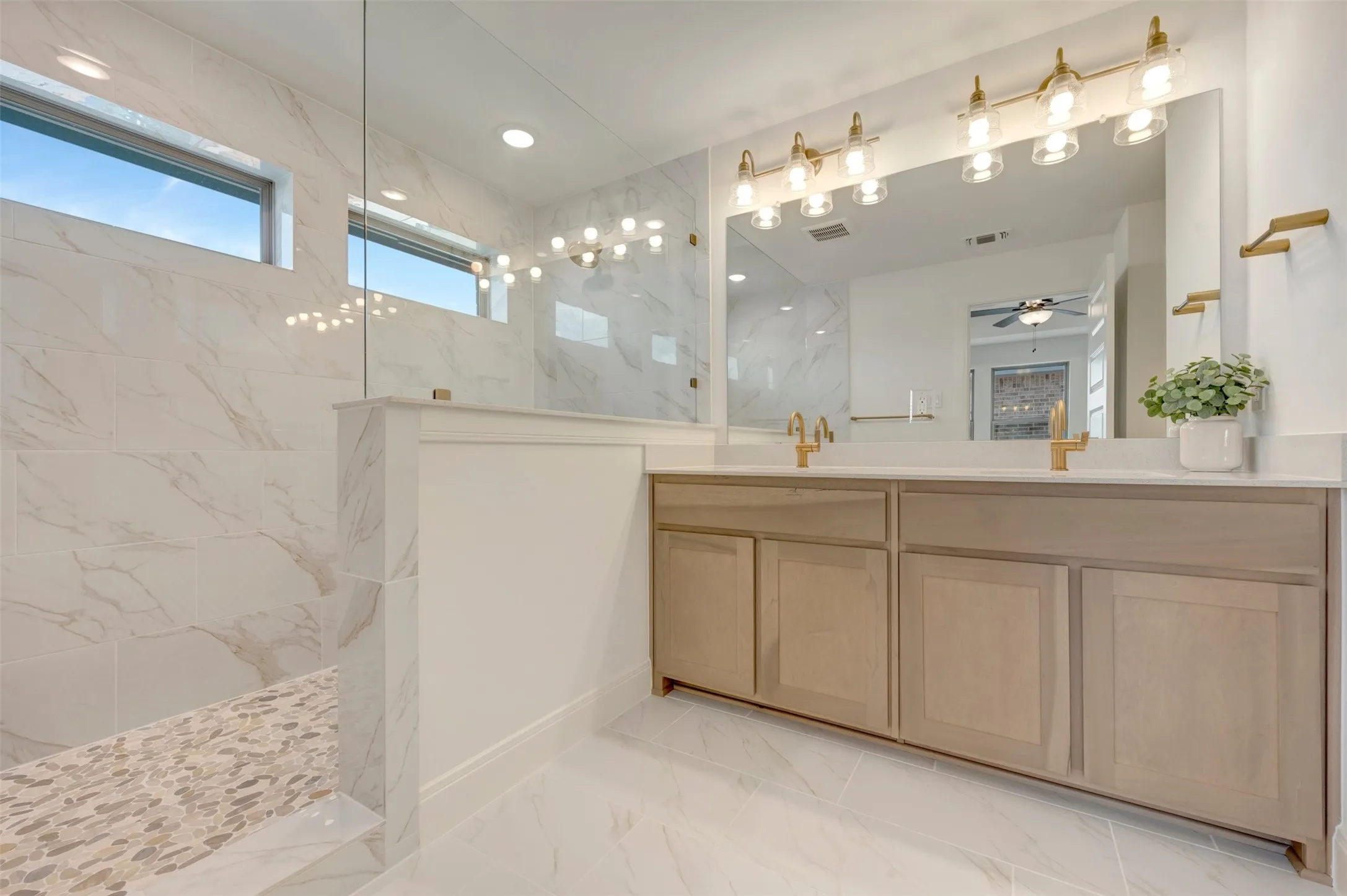 Contemporary bathroom featuring a dual vanity with light wood-finish cabinetry, a large vanity mirror, and gold-tone fixtures