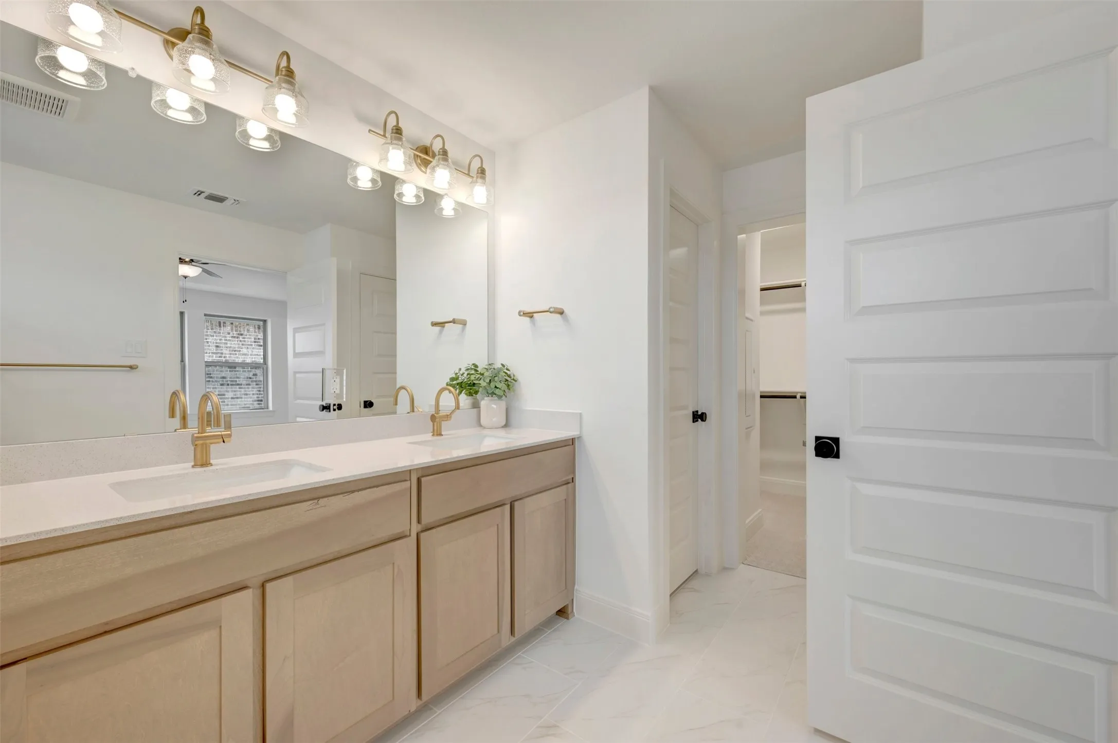 Dual vanity with light wood-finish cabinetry, white countertops, and gold-toned fixtures