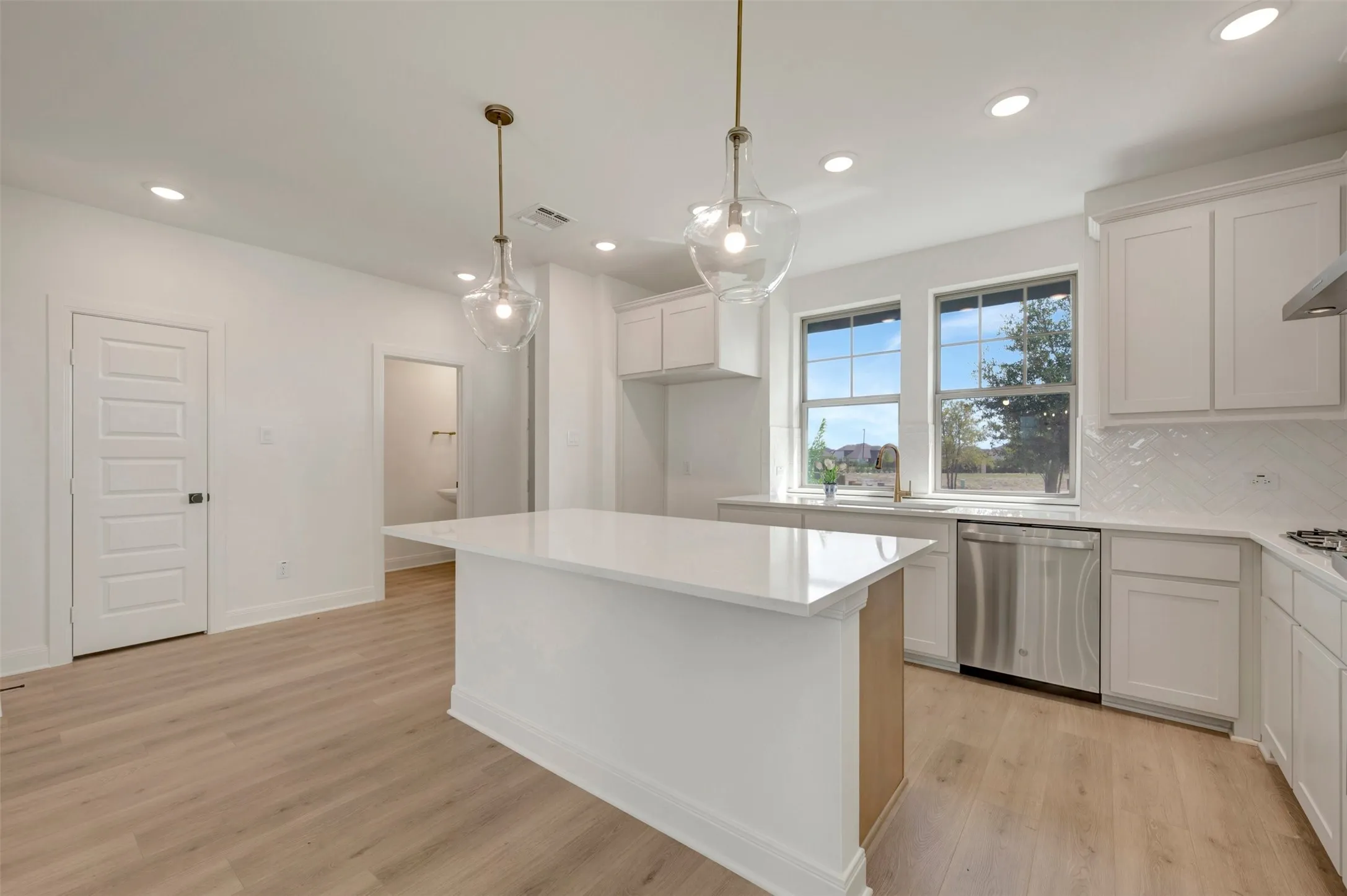 Modern kitchen featuring a central island with a solid surface countertop, recessed lighting, and two clear glass pendant lights