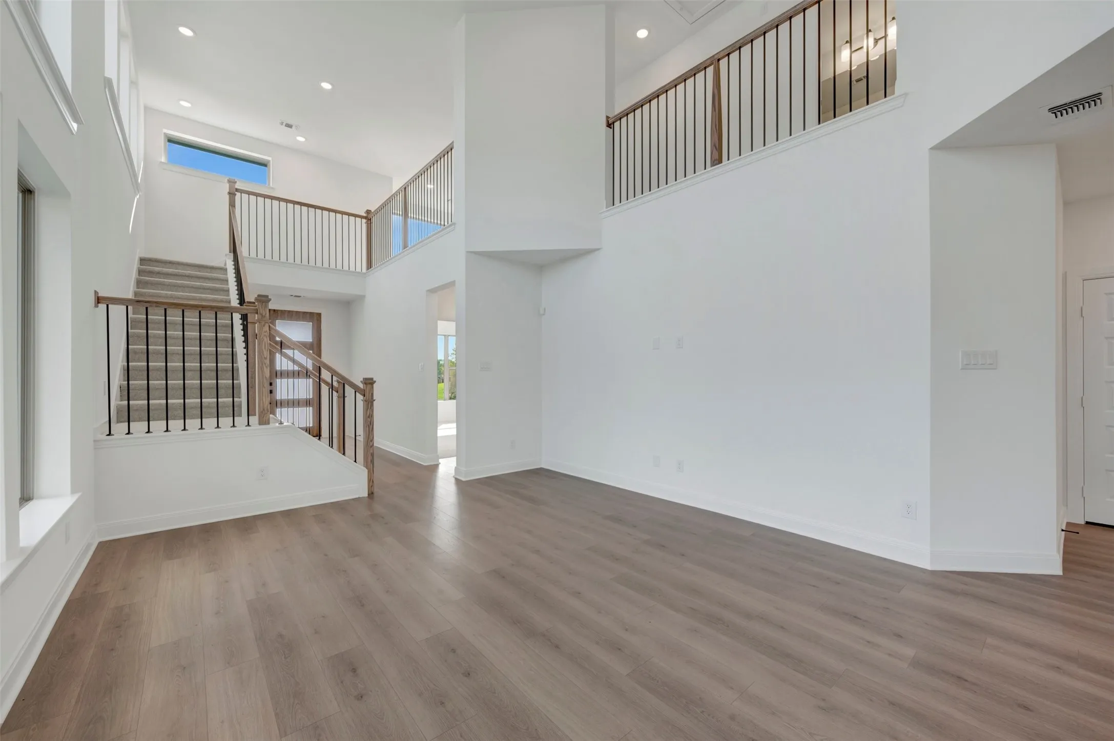 Two-story foyer featuring a grand staircase with wood-finish handrails and black metal balusters, wood-finish flooring, and high ceilings with recessed lighting