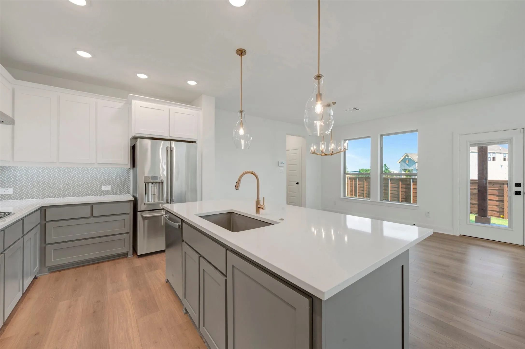 Modern kitchen featuring a large central island with a sink, white countertops, two-tone cabinetry, stainless steel appliances, and wood-finish flooring