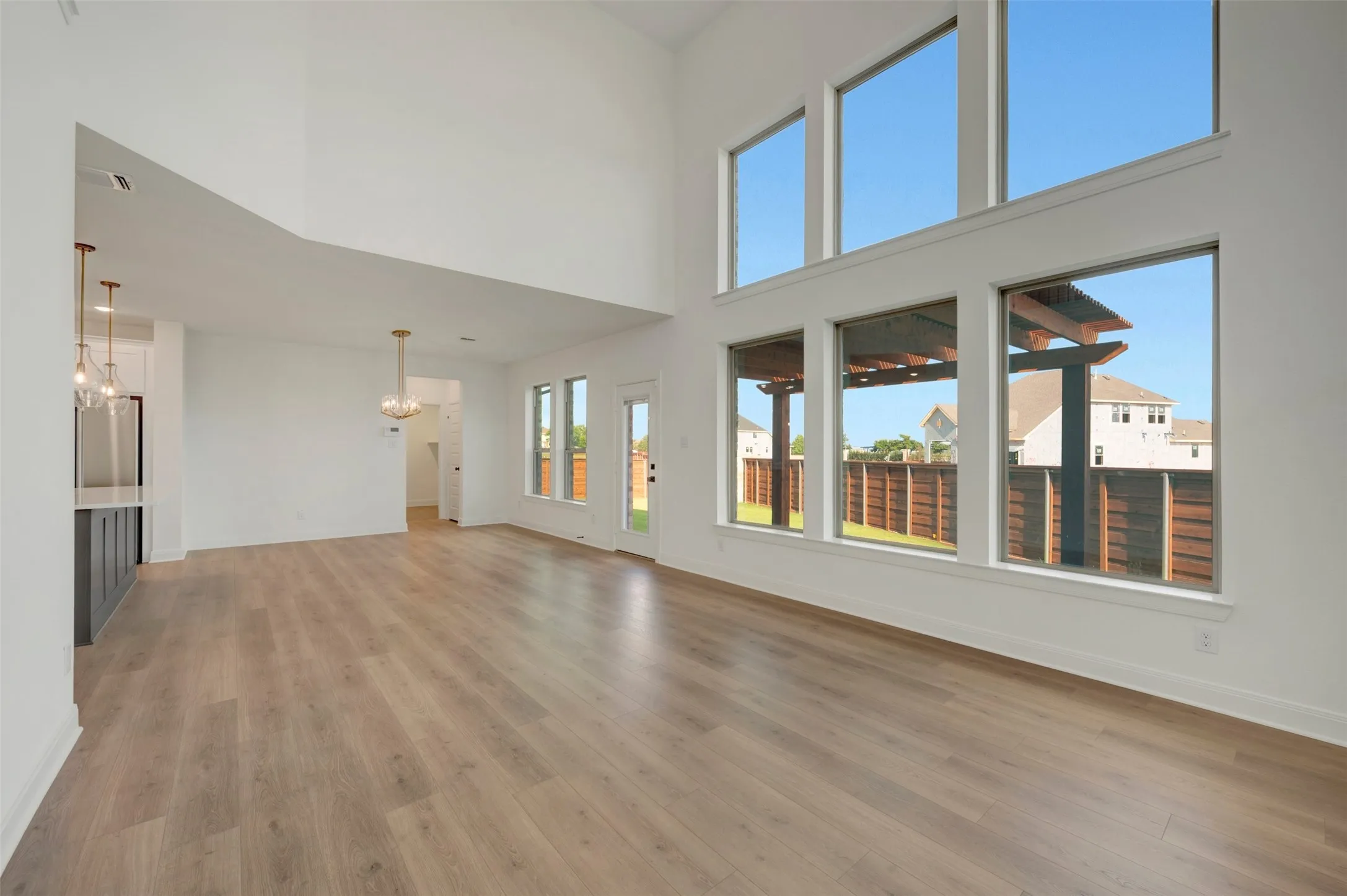 Spacious living area featuring high ceilings, wood-finish flooring, a wall of large windows, and a built-in wet bar with pendant lighting