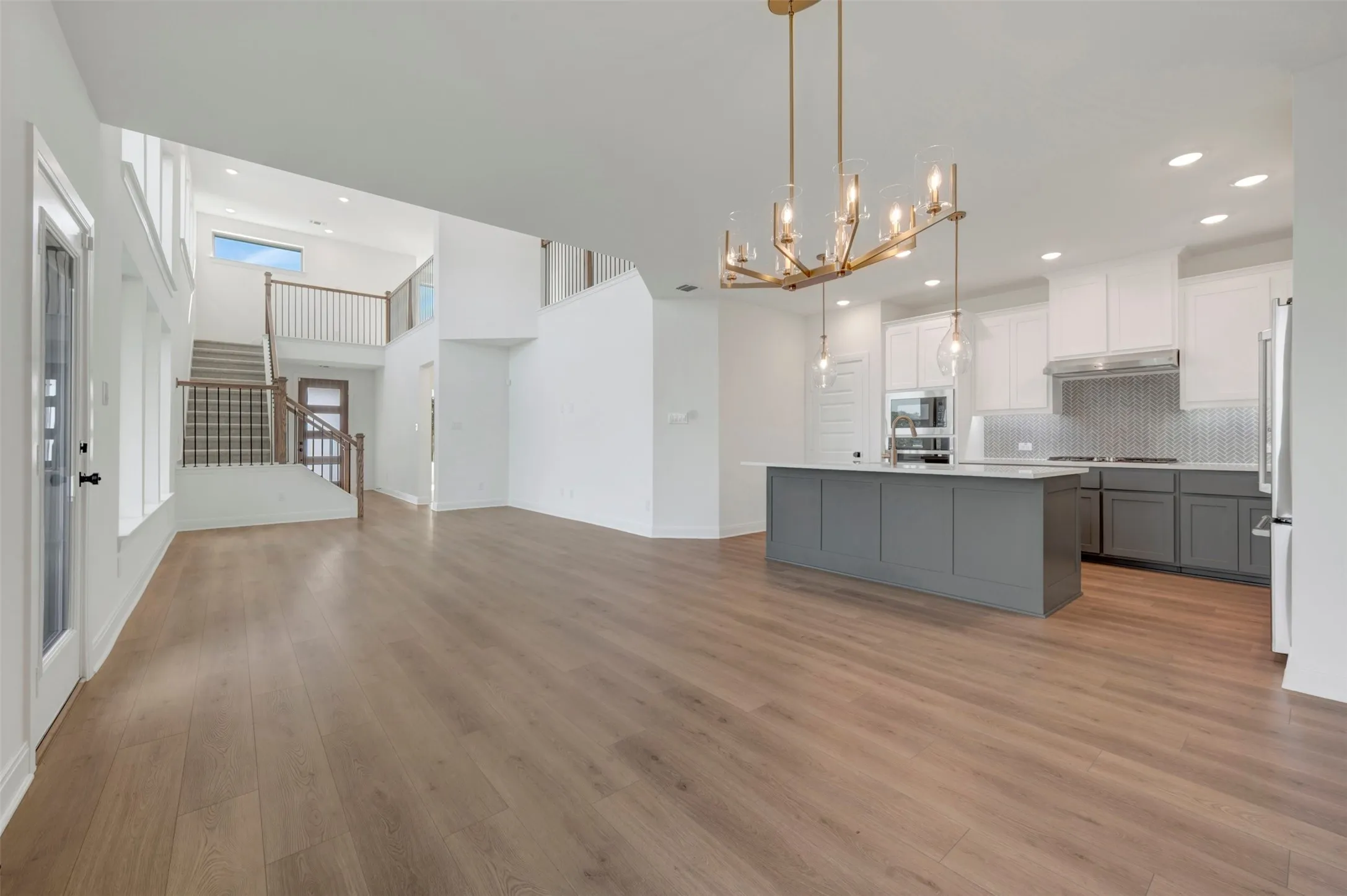 Open-concept living area with wood-finish flooring, a contemporary kitchen, and a striking two-story entryway