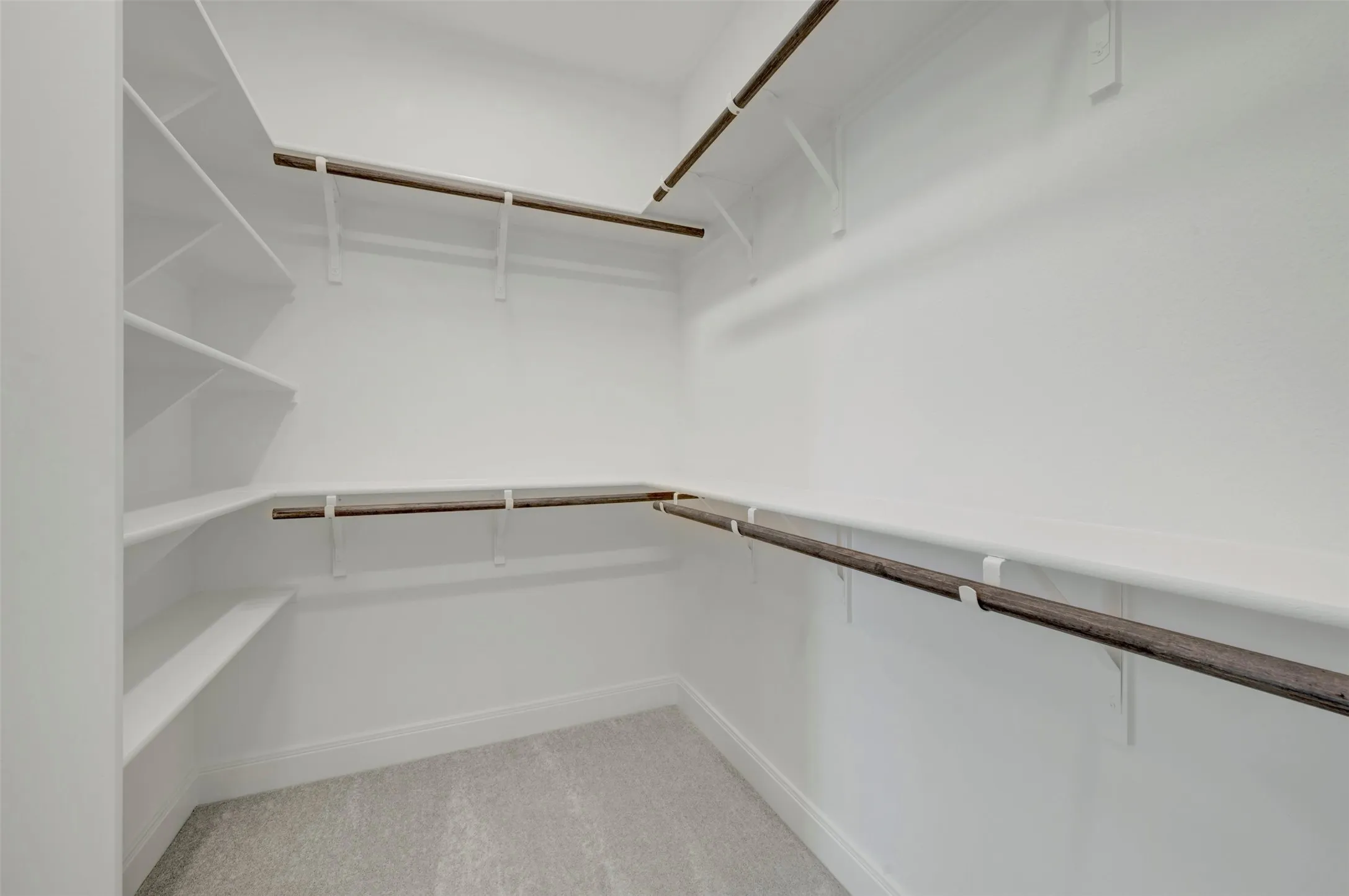 Walk-in closet featuring light gray carpet, white walls, multiple shelving units, and multiple clothing rods
