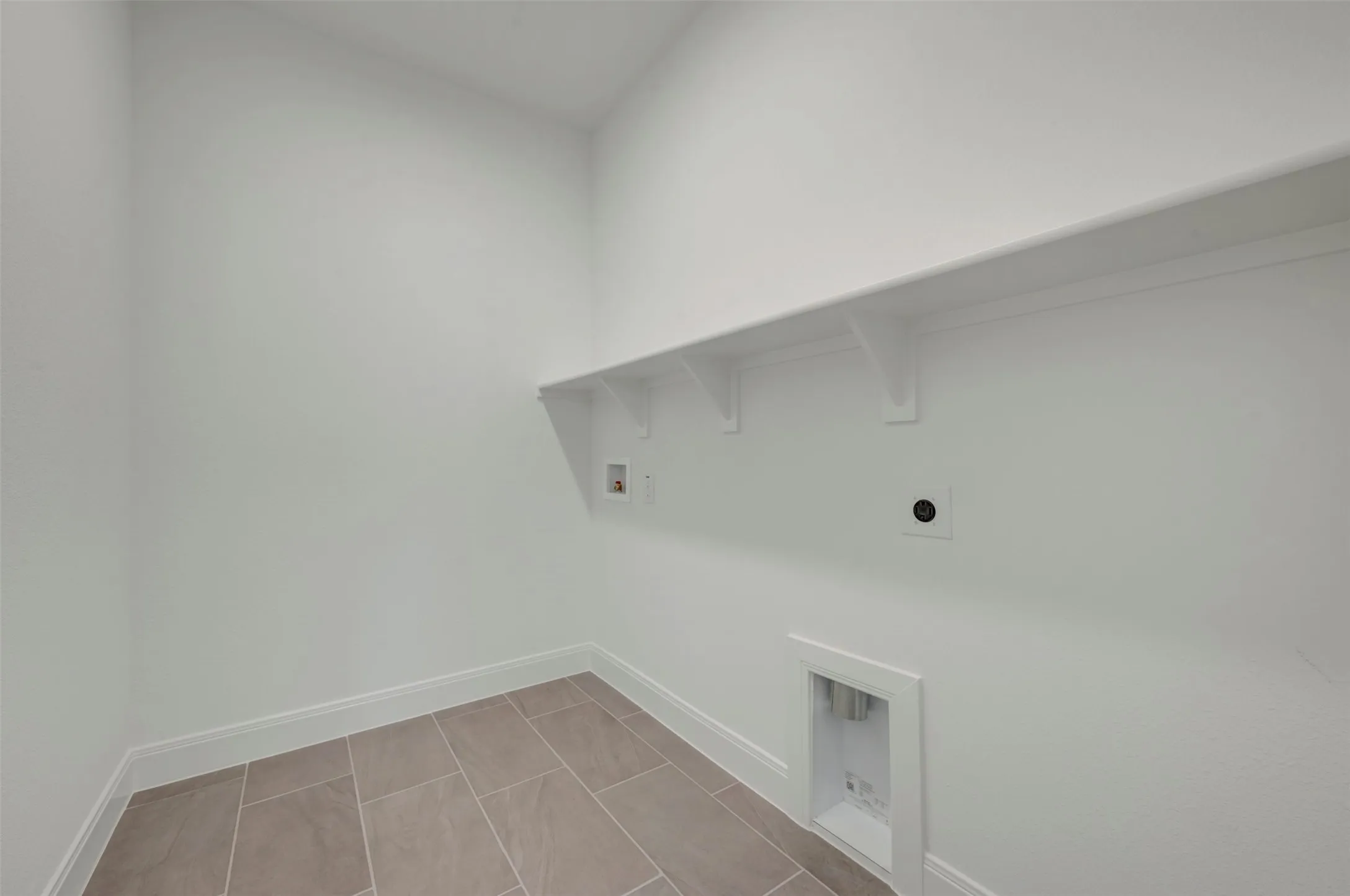 Utility area featuring a built-in shelf, neutral wall paint, tile flooring, and a baseboard trim