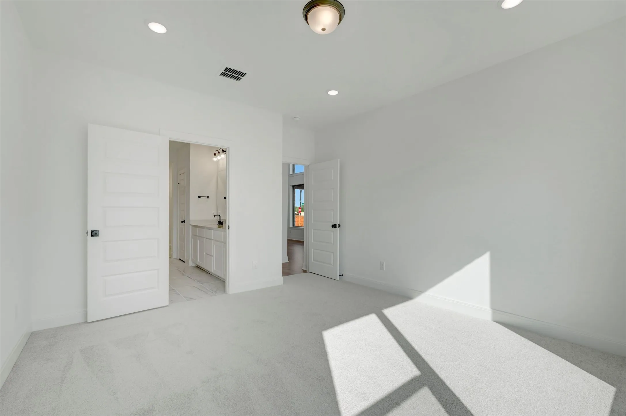 Spacious interior room featuring light-colored carpeting, white walls, and recessed lighting