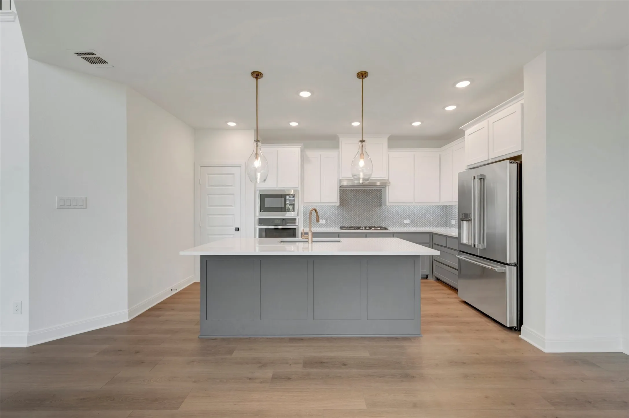 Modern kitchen featuring a central island with a light-toned countertop, pendant lighting, stainless steel appliances, white upper cabinetry, and gray lower cabinetry