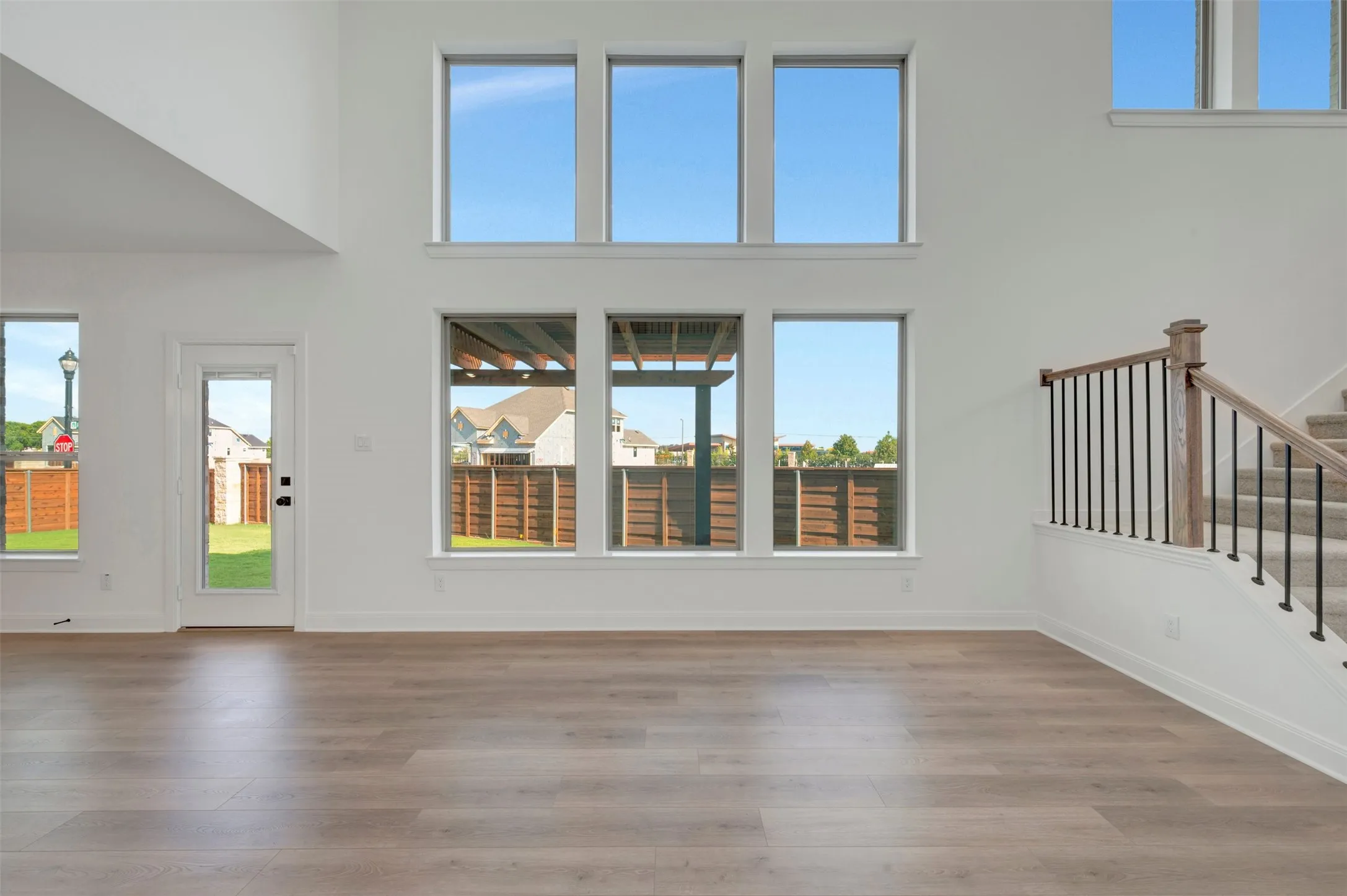Spacious interior featuring soaring ceilings, abundant natural light from multiple windows, wood-finish flooring, and a contemporary staircase with dark metal spindles and a wood handrail
