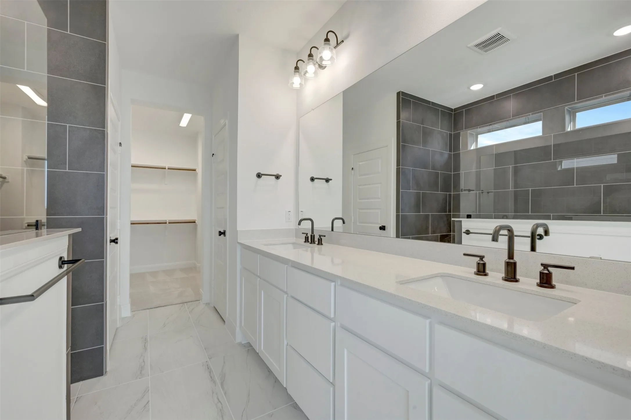 Bathroom featuring a double vanity with white cabinetry, integrated sinks, bronze-finish faucets, and an expansive mirror