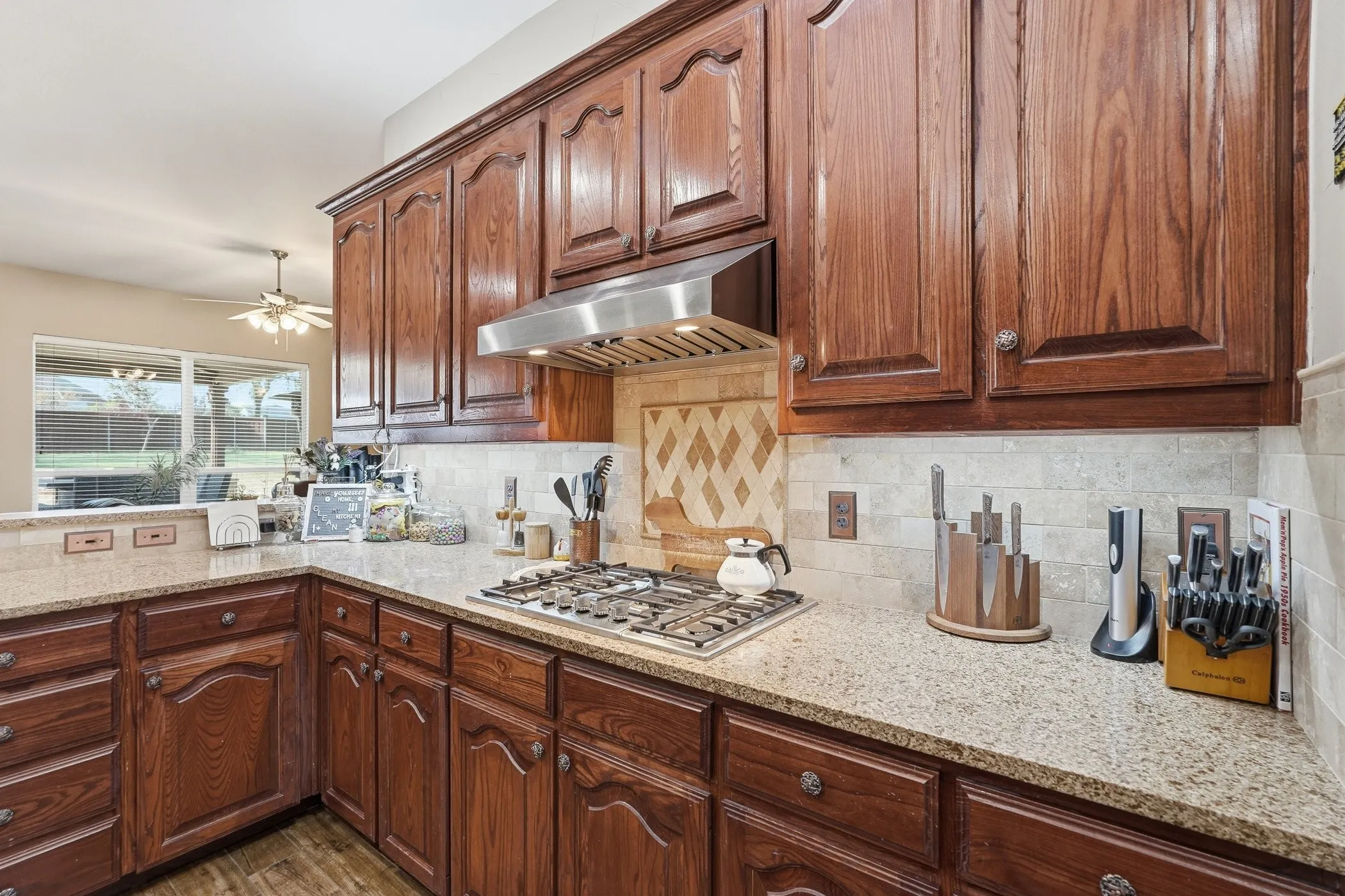 Kitchen with light stone countertops, stainless steel gas stovetop, tasteful backsplash, and a ceiling fan