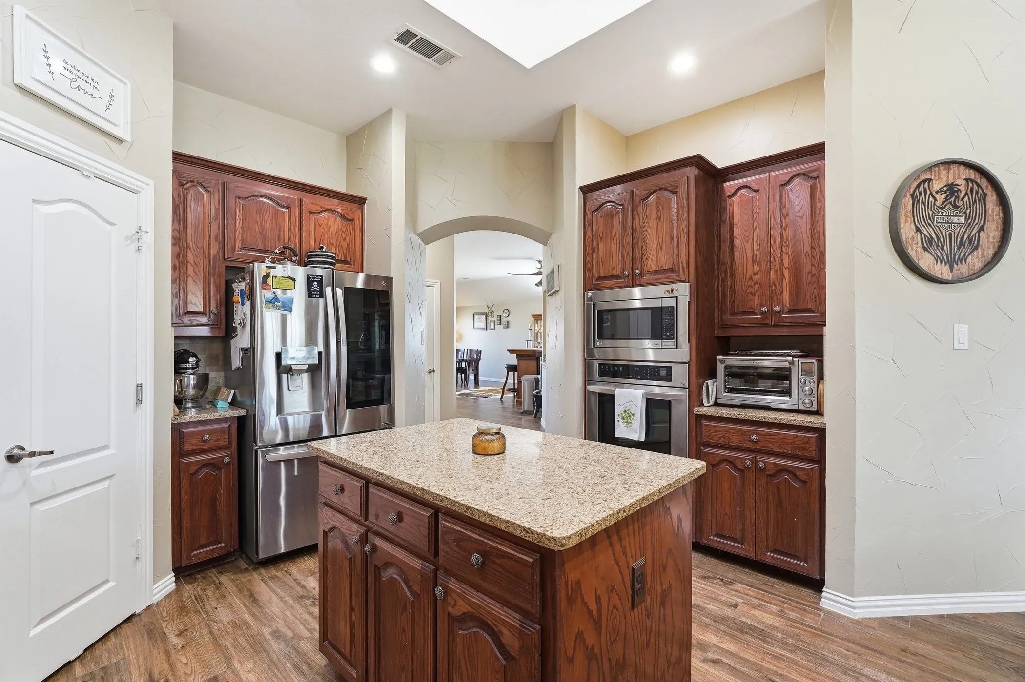 Kitchen featuring stainless steel appliances, a kitchen island, arched walkways, light stone counters, and dark wood-style floors