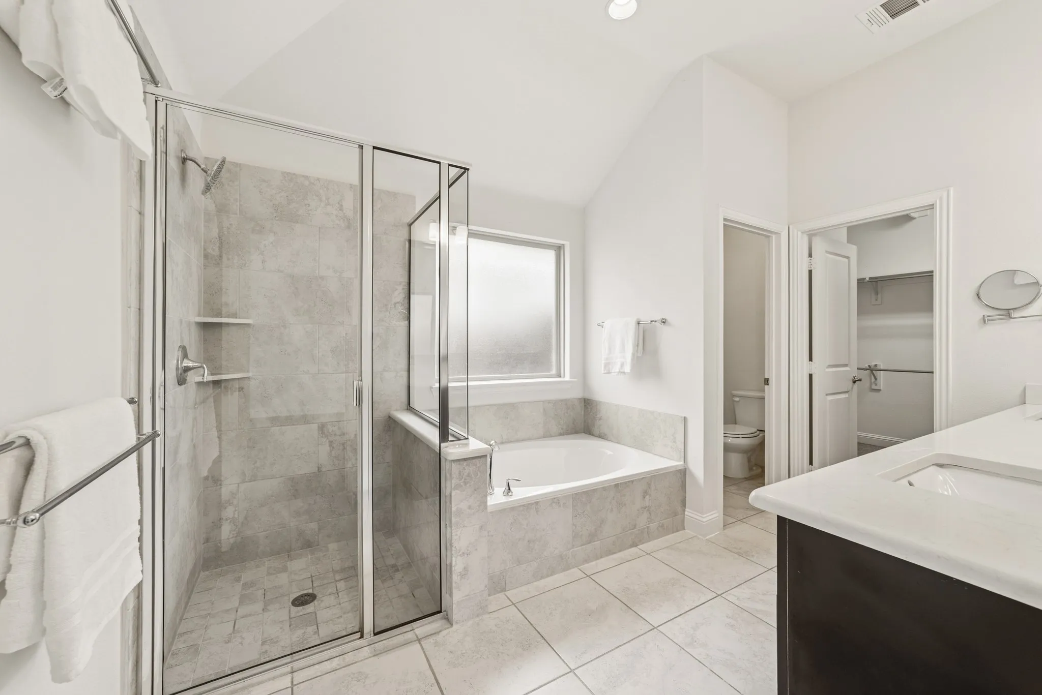 Bathroom featuring double vanity, a garden tub, a stall shower, vaulted ceiling, and light tile patterned flooring