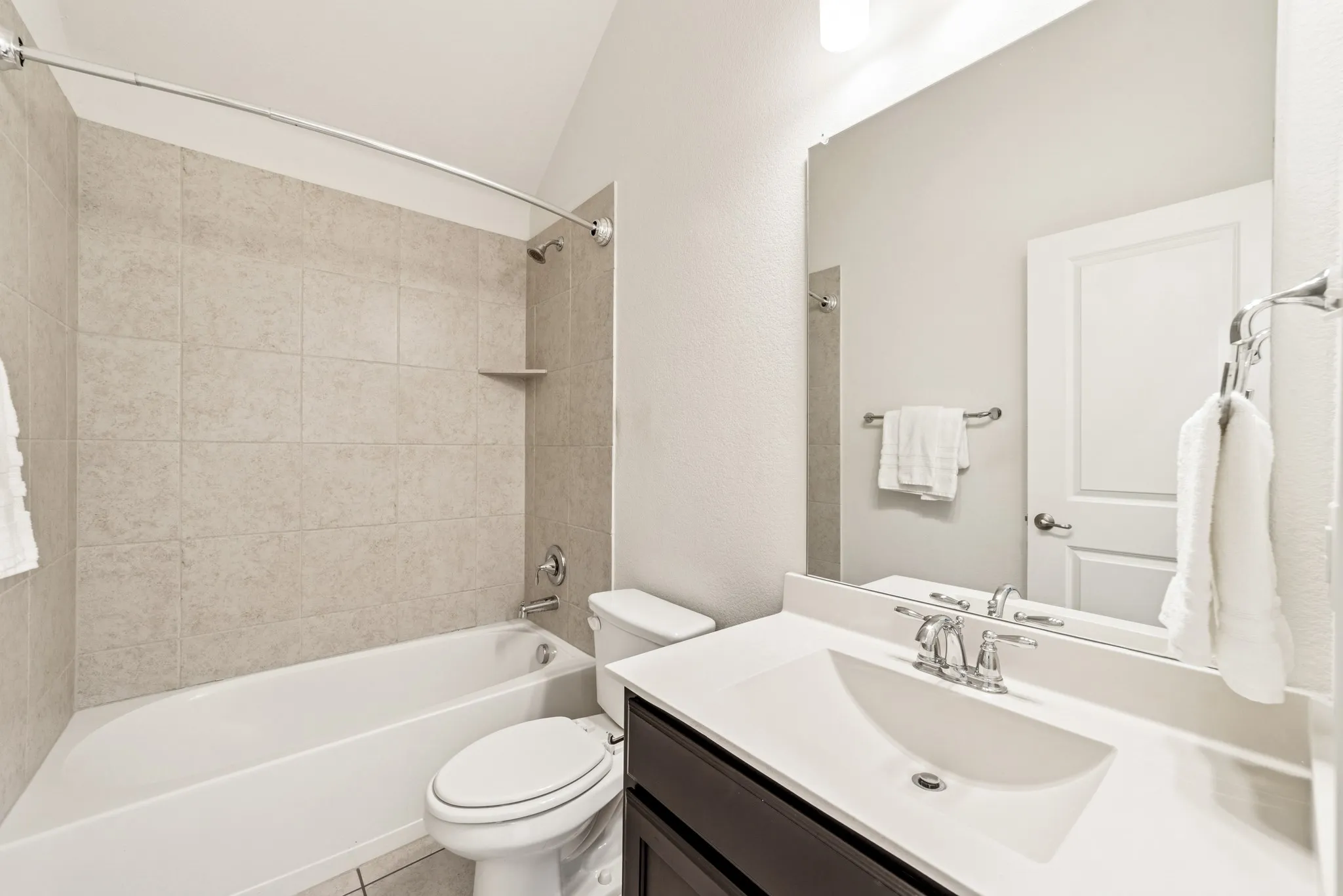 Bathroom with shower / bath combination, vanity, light tile patterned flooring, and vaulted ceiling