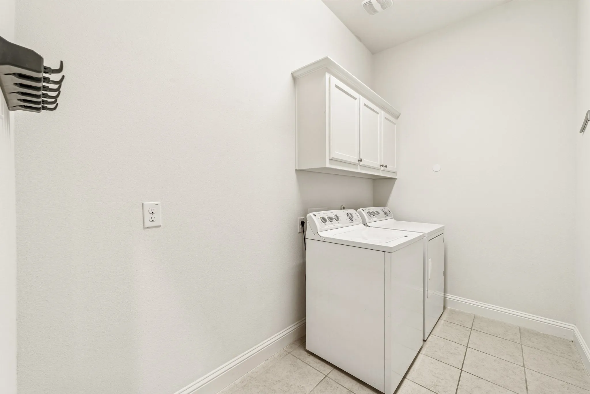 Laundry area featuring light tile patterned floors, cabinet space, and washing machine and clothes dryer