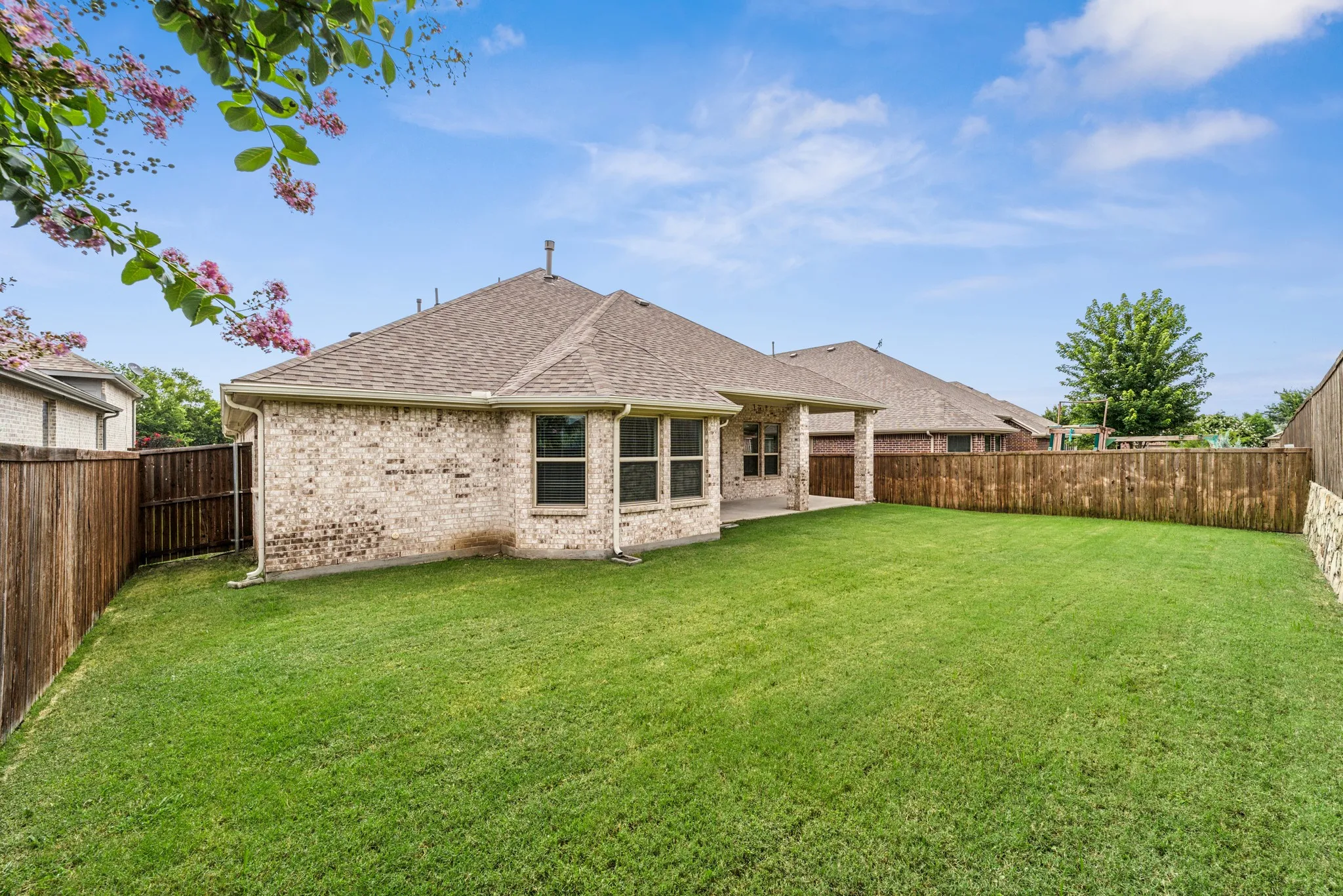 Rear view of property with a patio area, brick siding, a shingled roof, and a fenced backyard