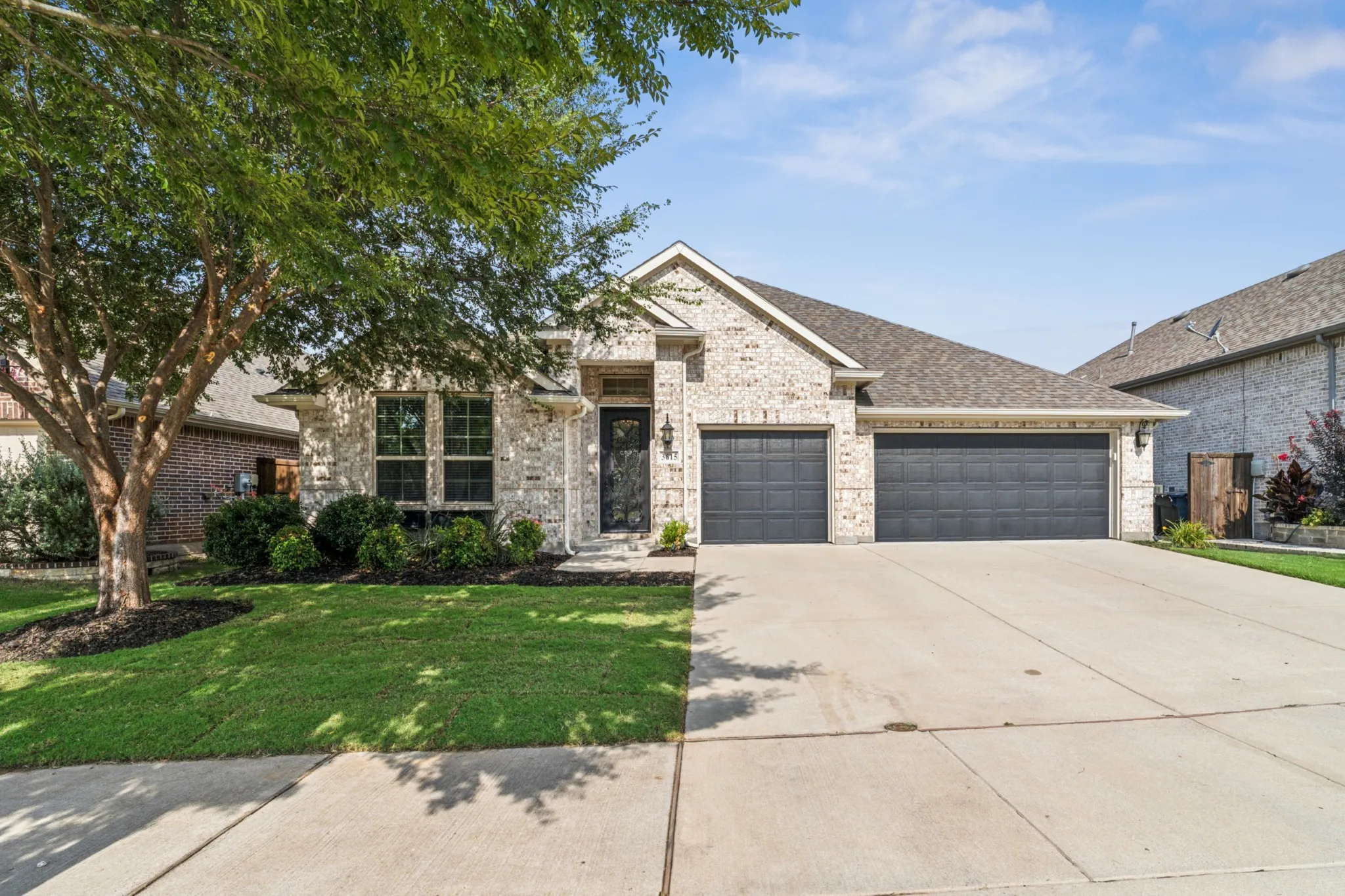 French country home with brick siding, driveway, a 3-car garage, and a front yard