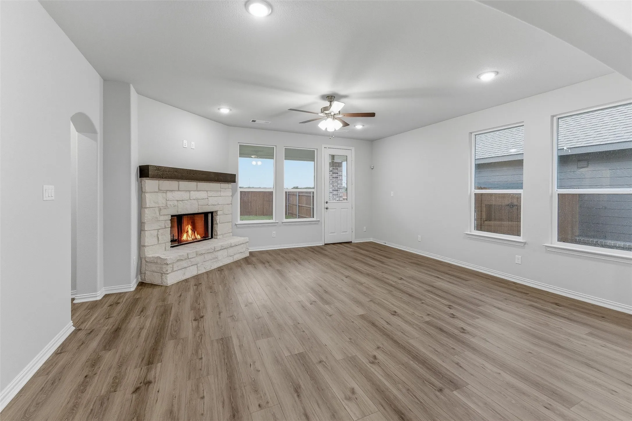 Spacious living area featuring wood-finish flooring, a stone fireplace with a substantial mantel, a ceiling fan, recessed lighting, and multiple windows