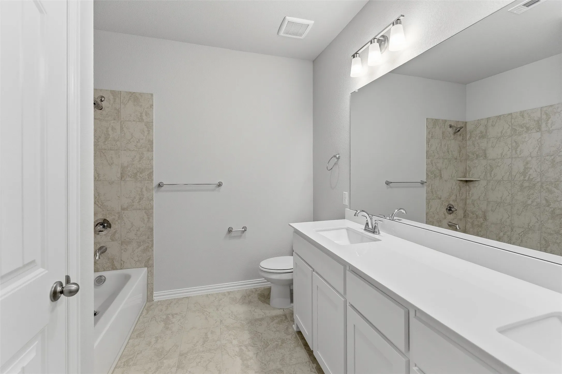 Bathroom featuring a double vanity with white cabinetry and integrated sinks, a full-width mirror, and a bathtub with tiled surround