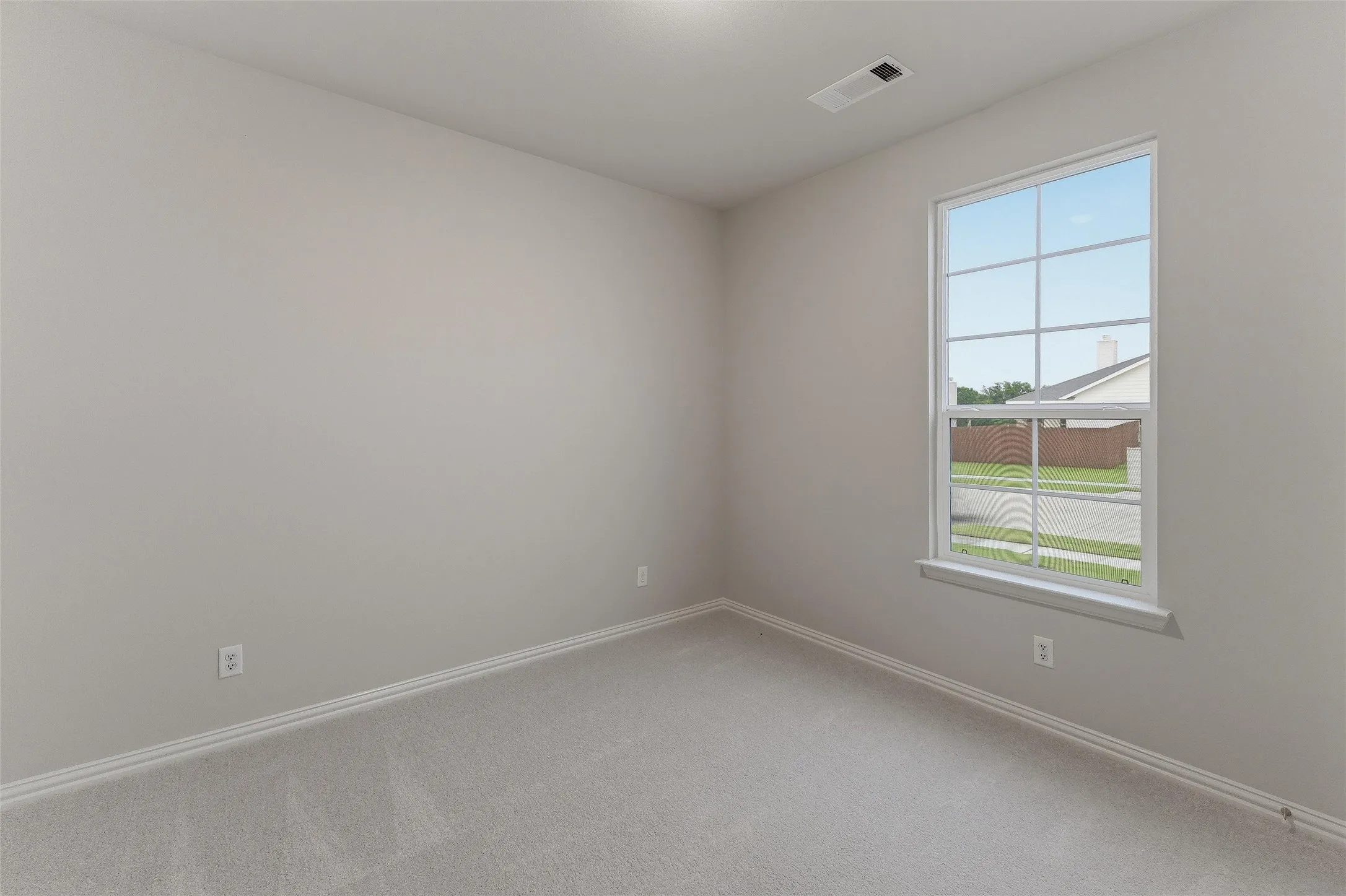 Neutral-toned room featuring a large window with grid pattern, light gray carpeting, matching baseboards, and a ceiling-mounted light fixture