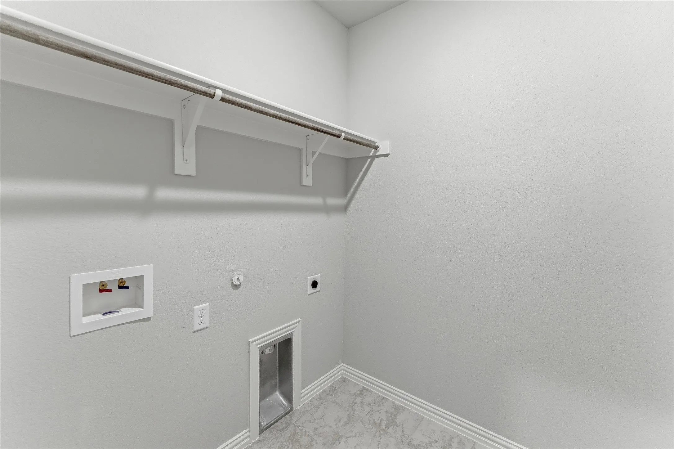 Dedicated laundry space featuring a built-in shelf, hanging rod, and base trim