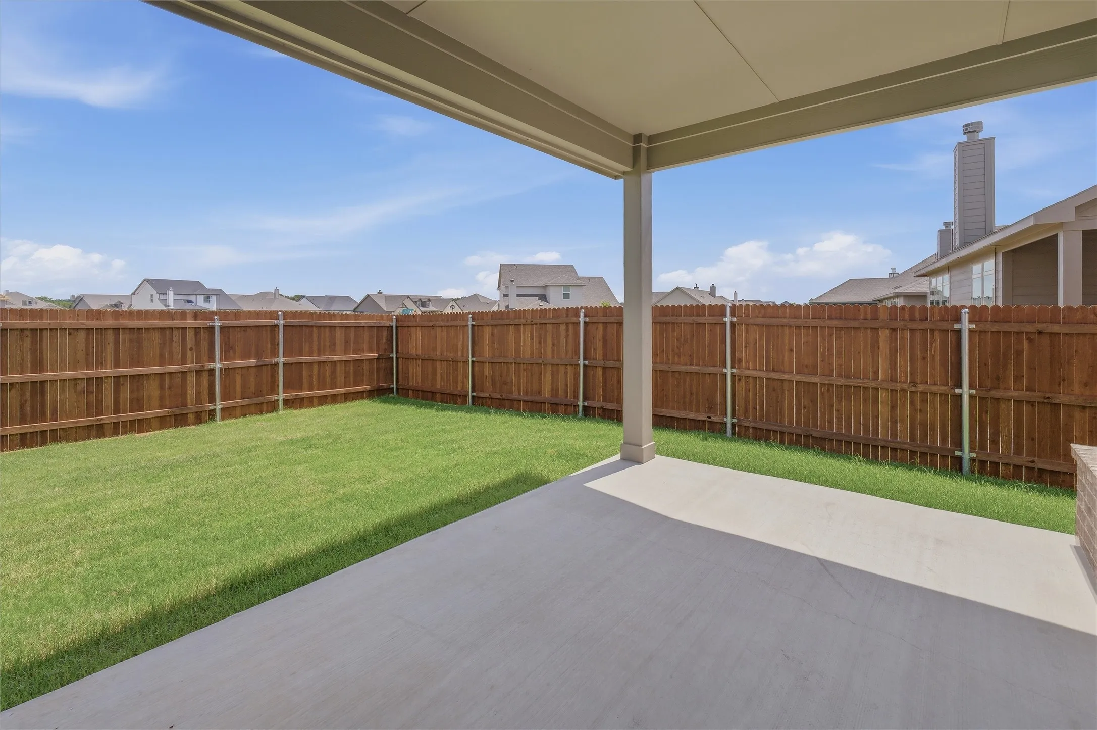 Covered concrete patio opening to a fenced rear yard with a manicured lawn