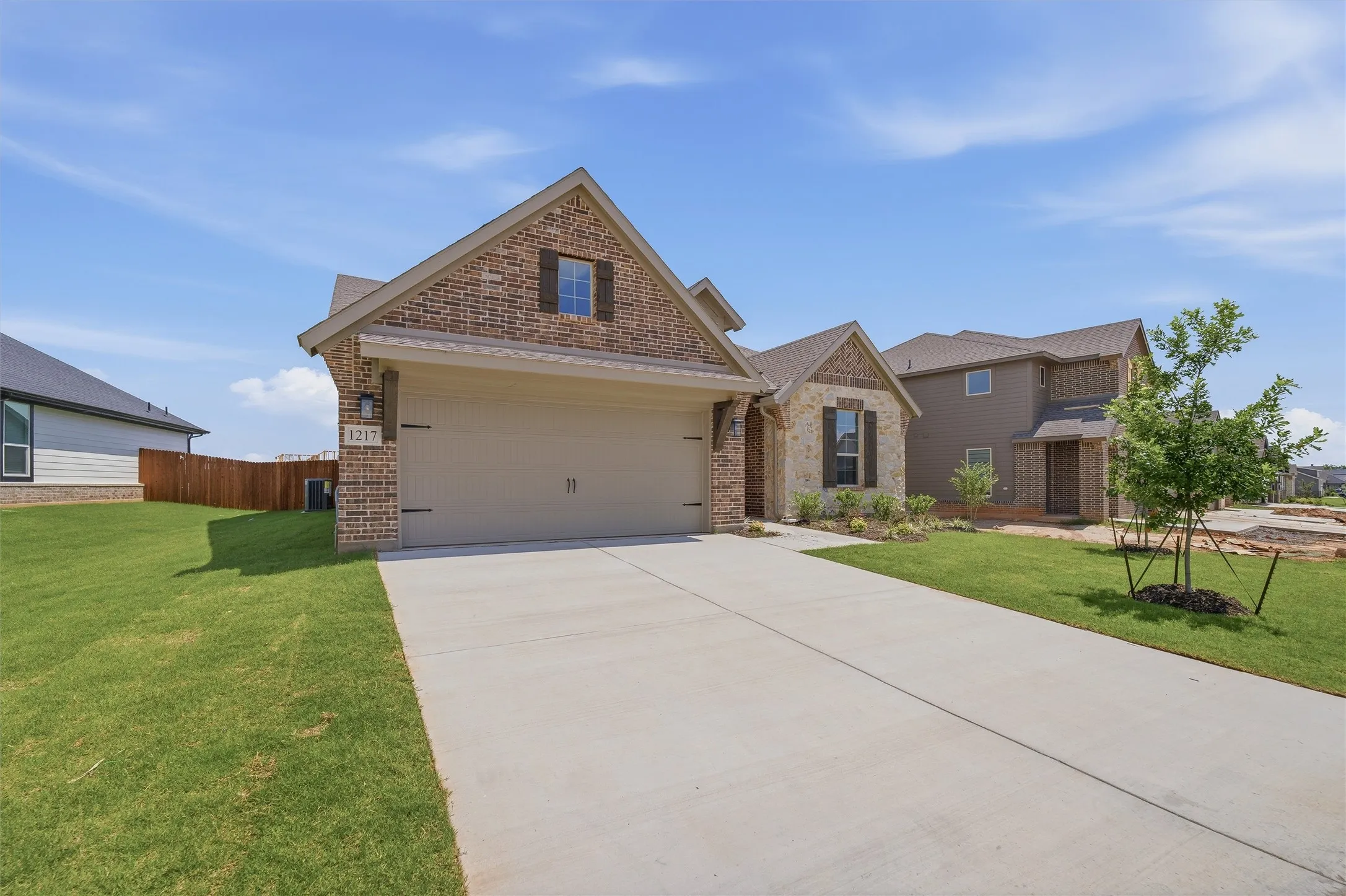 Brick and stone façade with an attached garage, concrete driveway, and front landscaping