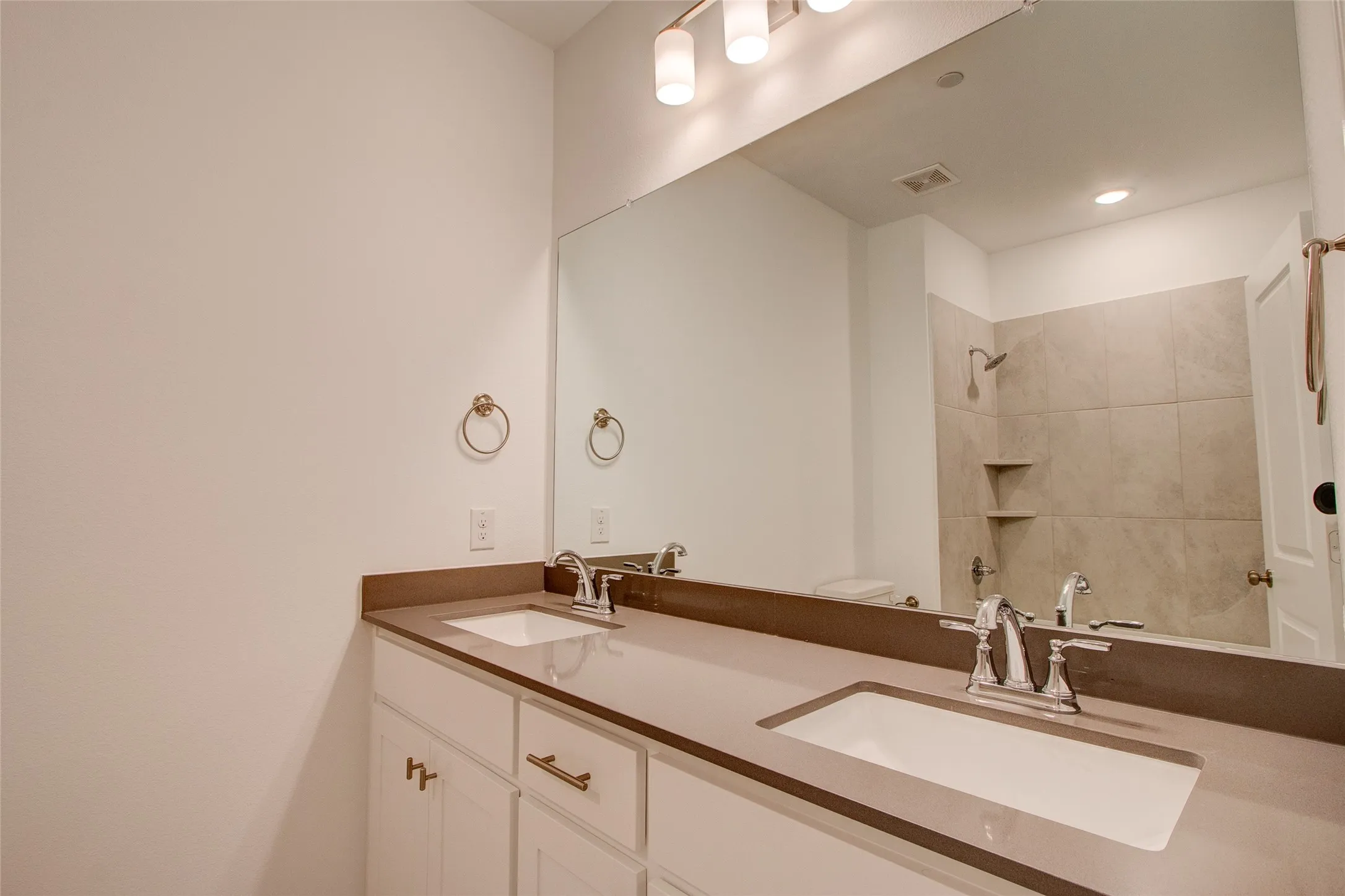 Full bath with double vanity, a tile shower, and recessed lighting