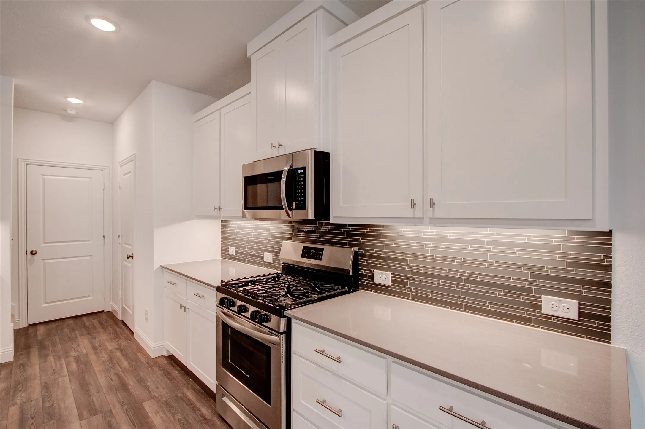 Kitchen with stainless steel appliances, white cabinets, dark wood-style flooring, tasteful backsplash, and recessed lighting