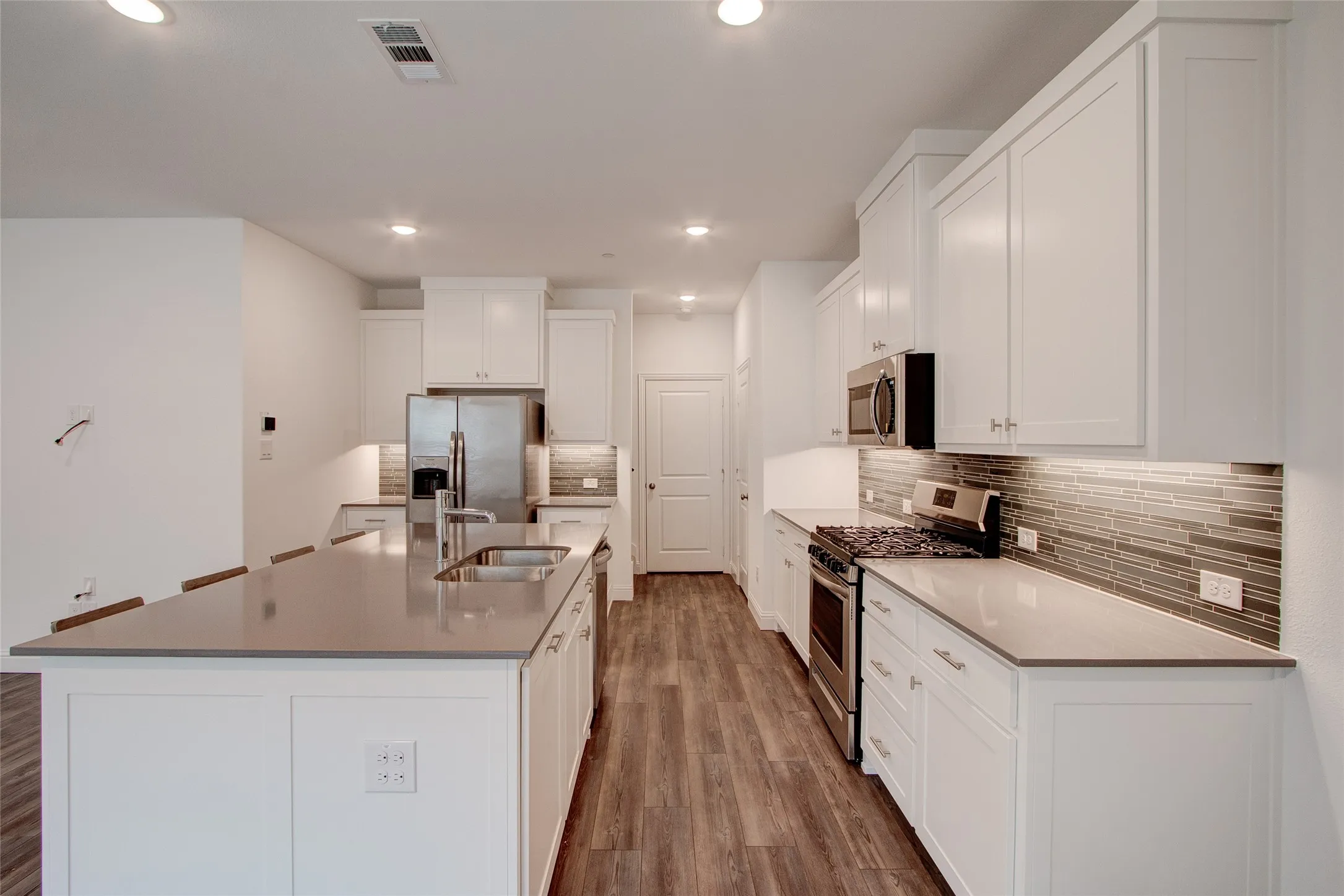 Kitchen with stainless steel appliances, white cabinetry, dark wood-type flooring, backsplash, and recessed lighting
