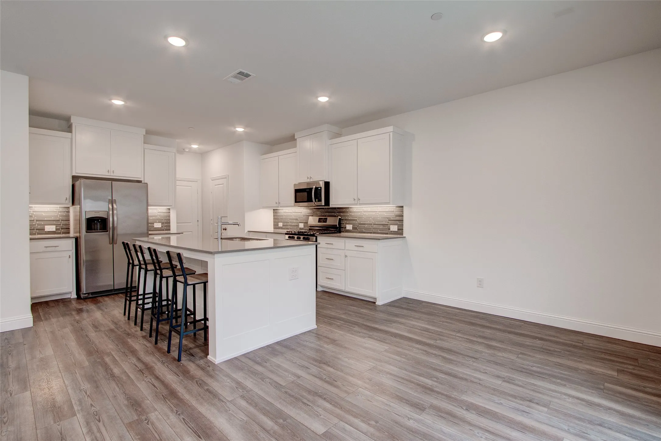 Kitchen featuring stainless steel appliances, white cabinets, a breakfast bar area, an island with sink, and recessed lighting