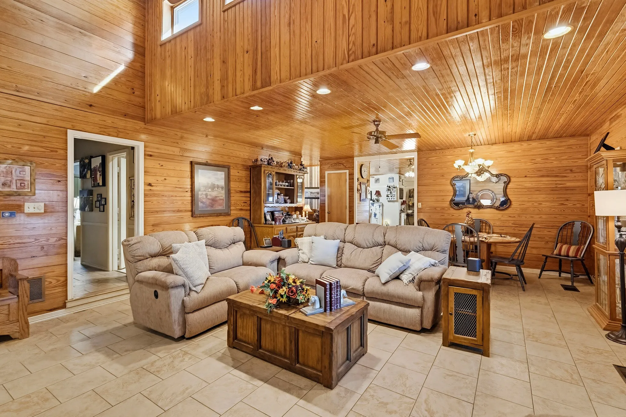 Living room featuring wood walls, a ceiling fan, hanging lights, and a high wood ceiling